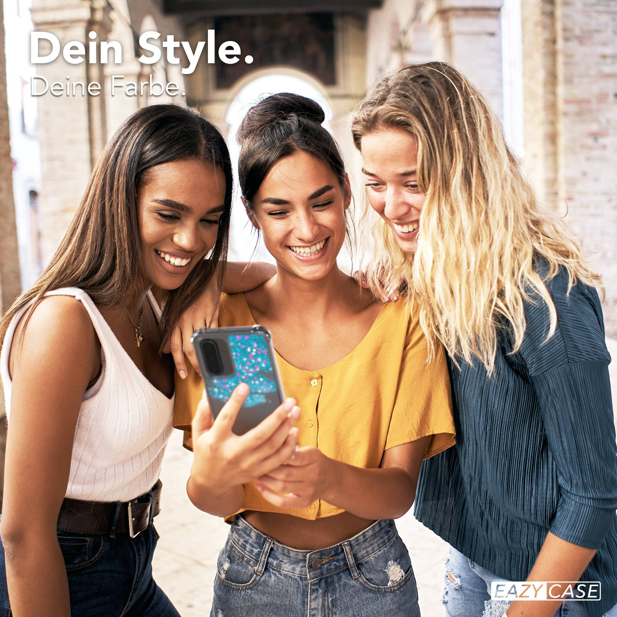 Drei junge Frauen lachen und schauen auf ein Handy mit blauem Glitzer-Cover.