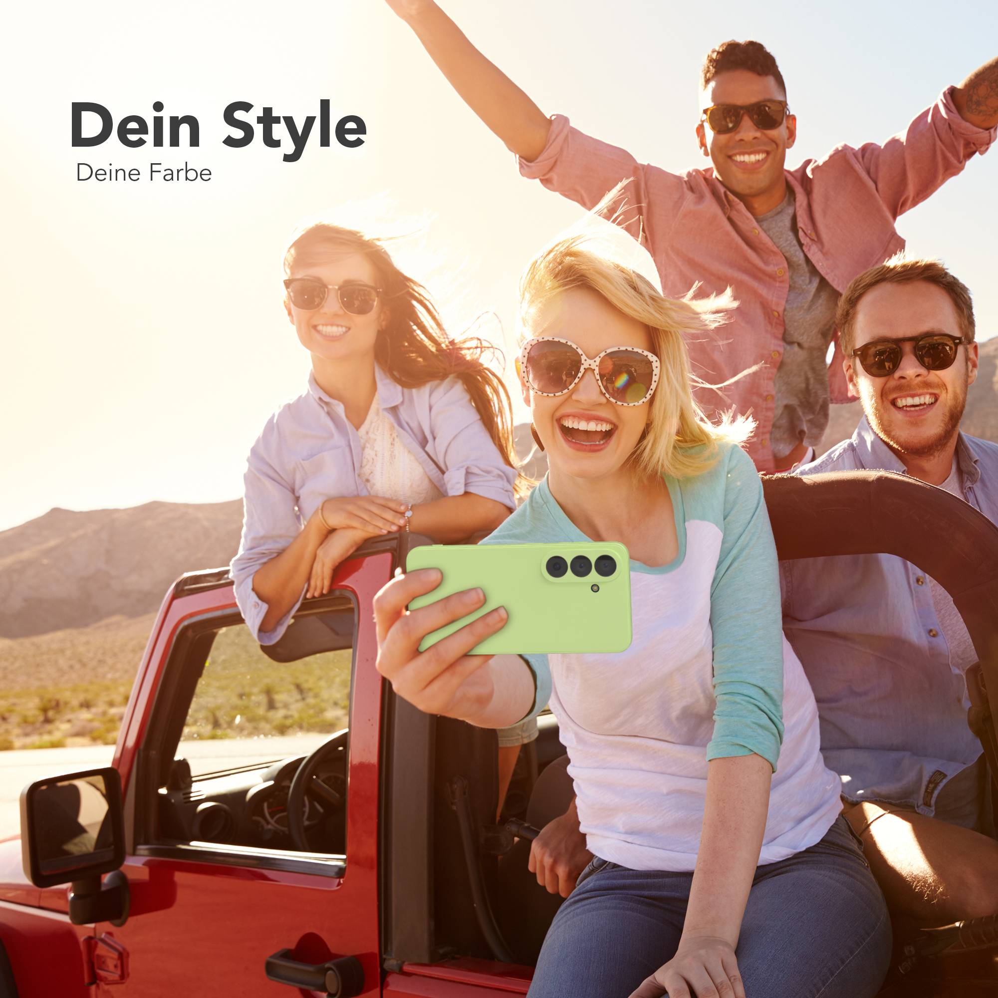 Vier Freunde machen ein Selfie in einem roten Jeep in sonniger Wüste.