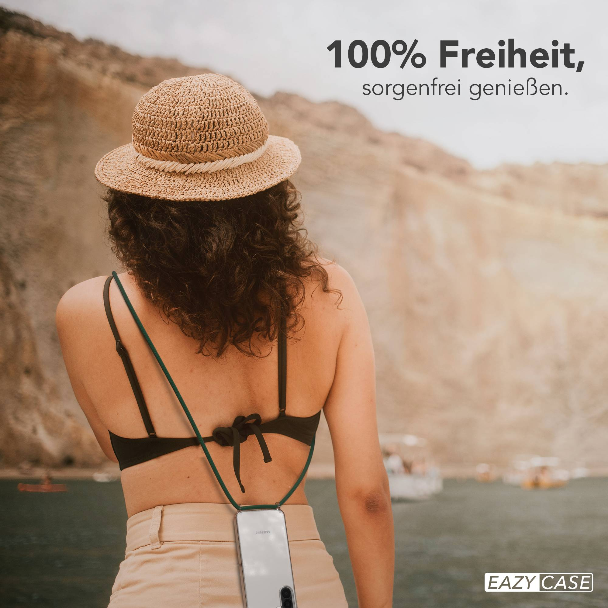 Frau mit Strohhut und Handy-Halterung am Rücken, am Wasser.