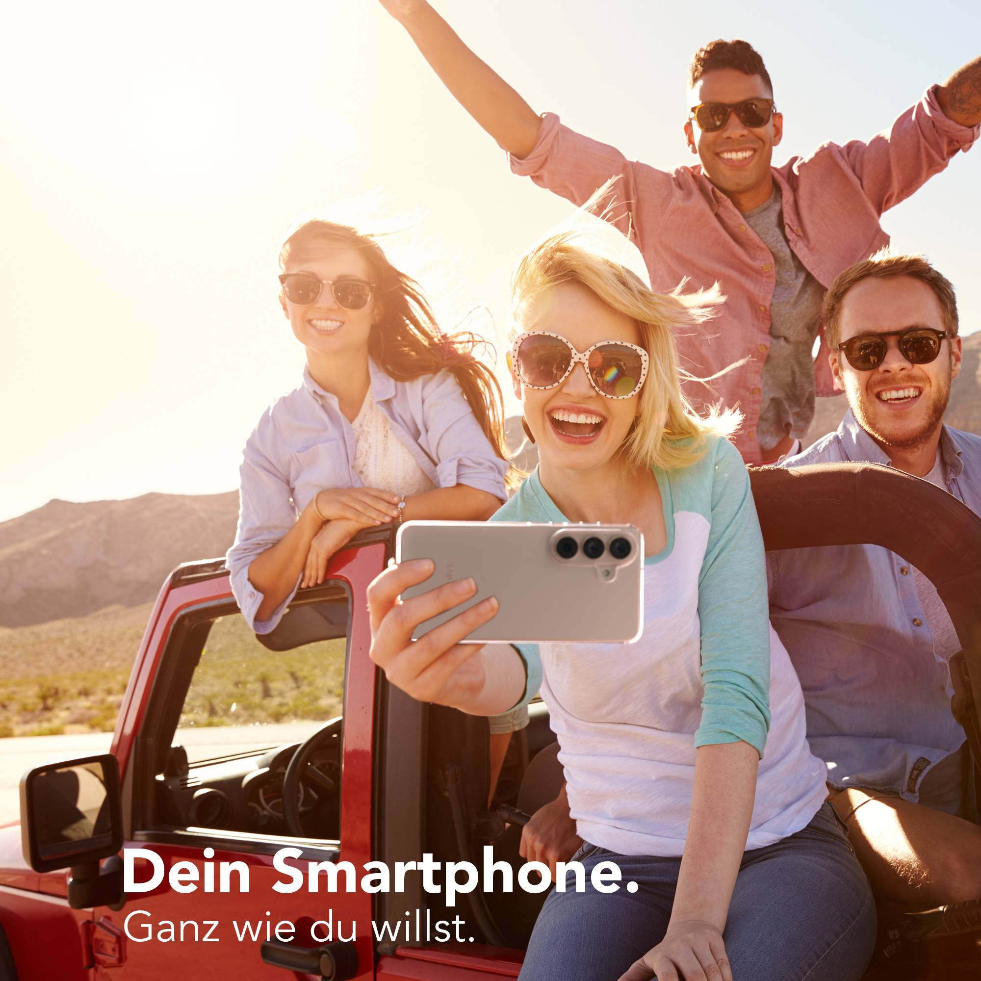 Vier Freunde im roten Jeep machen ein Selfie mit einem Smartphone bei Sonnenschein.