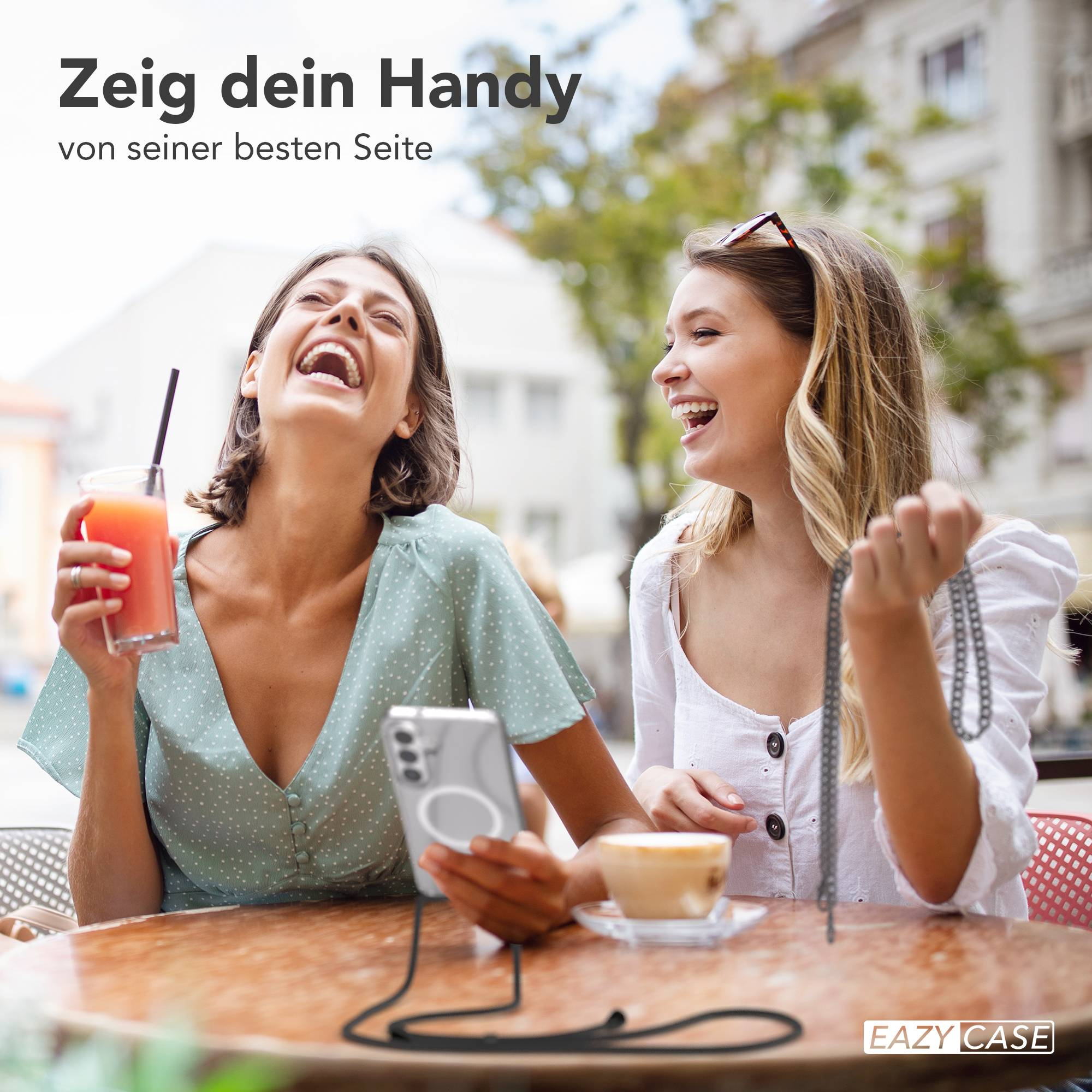 Zwei lachende Frauen sitzen draußen an einem Tisch mit Getränken.