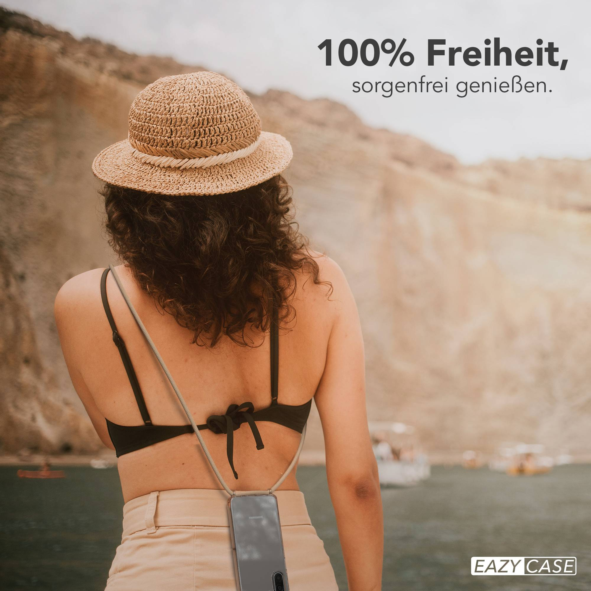 Frau mit Strohhut und Handy-Halterung am Rücken, am Wasser.