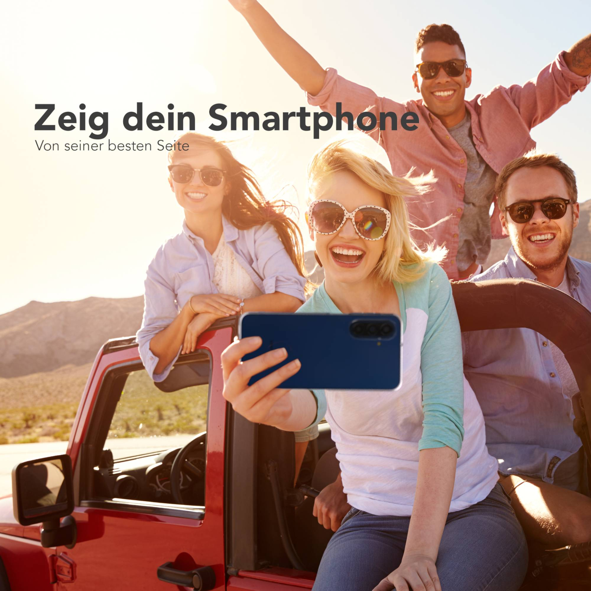 Vier junge Leute in einem roten Jeep, die Sonne scheint, sie lachen.