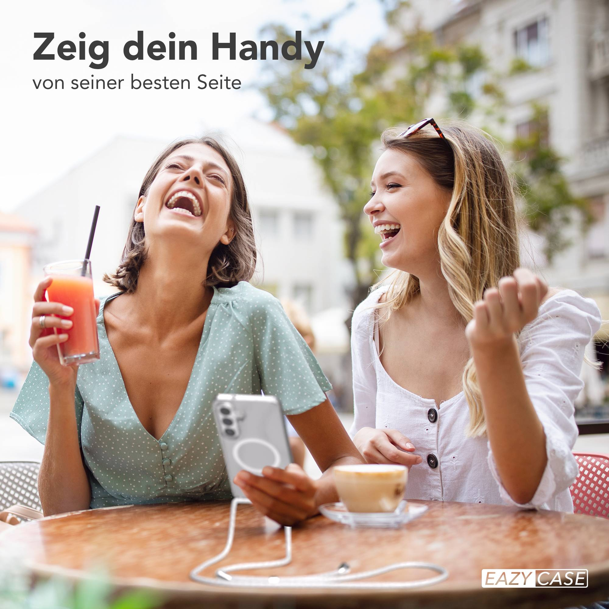 Zwei lachende Frauen sitzen an einem Tisch mit Getränken und einem Handy.