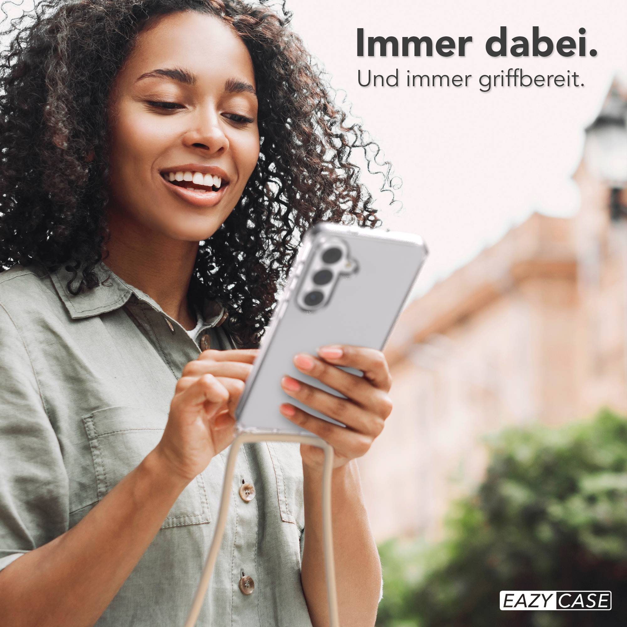 Frau mit lockigem Haar hält ein transparentes Handy mit einer Kordel.