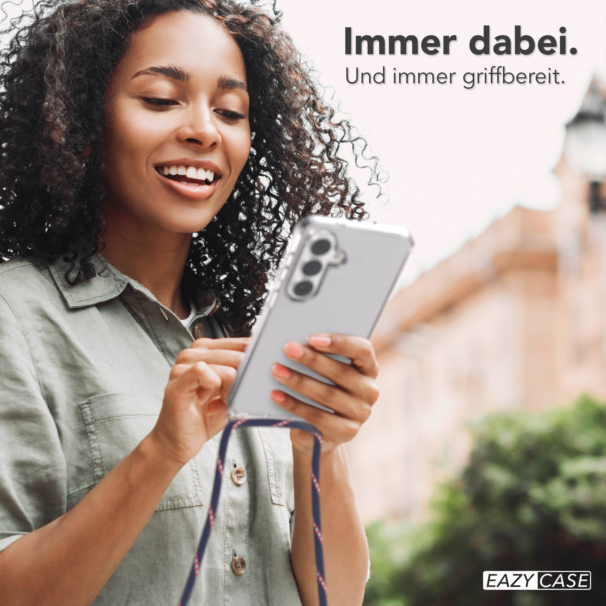 Frau mit Locken hält ein Smartphone mit Hülle und Schnur.
