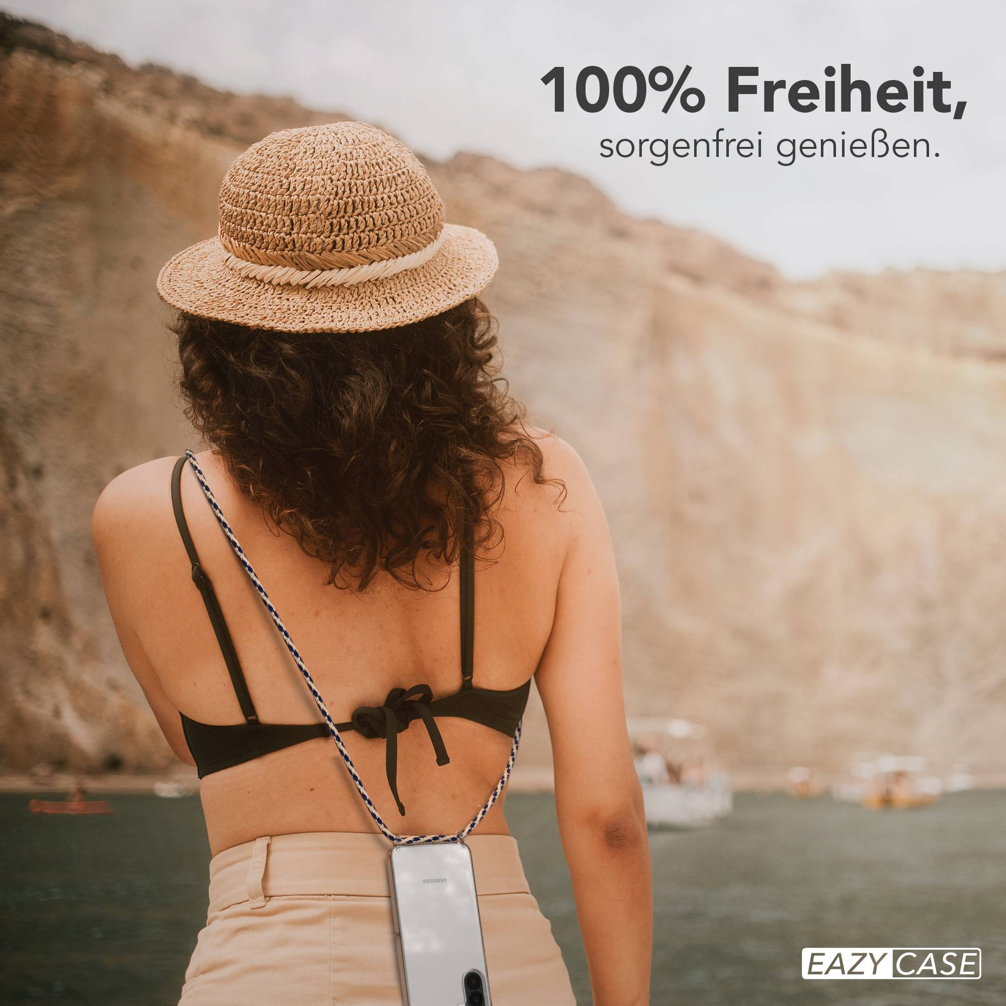 Frau mit Strohhut und Handy-Halskette am Meer.