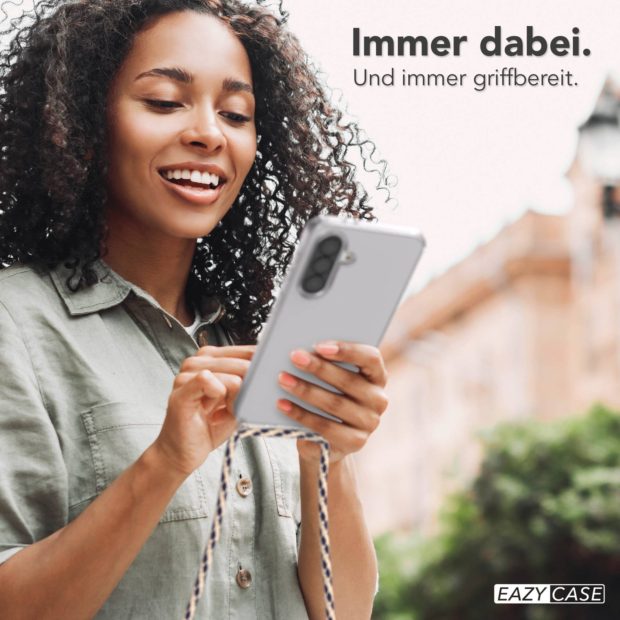 Frau mit lockigem Haar lächelt und hält ein transparentes Handycase mit einem Handy.