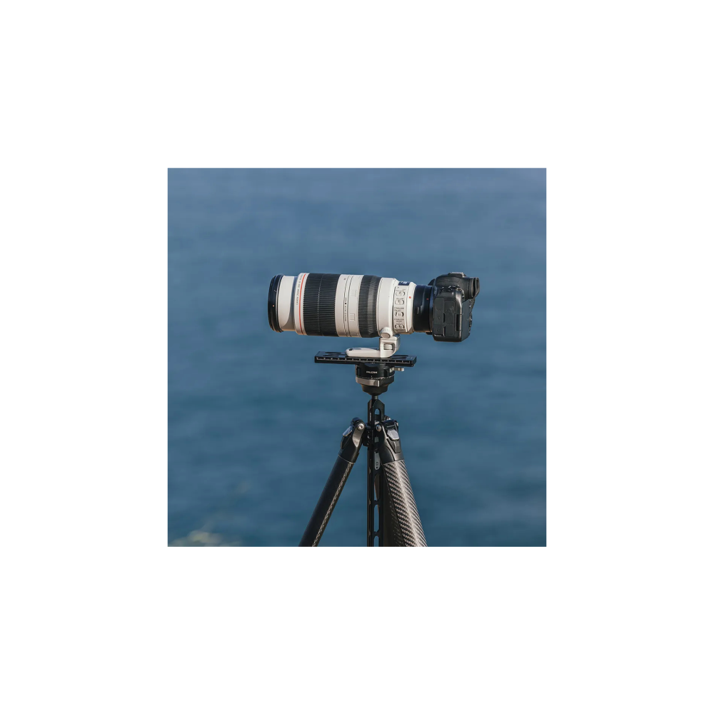 Een camera met een lange lens is op een statief gemonteerd, met de zee op de achtergrond.