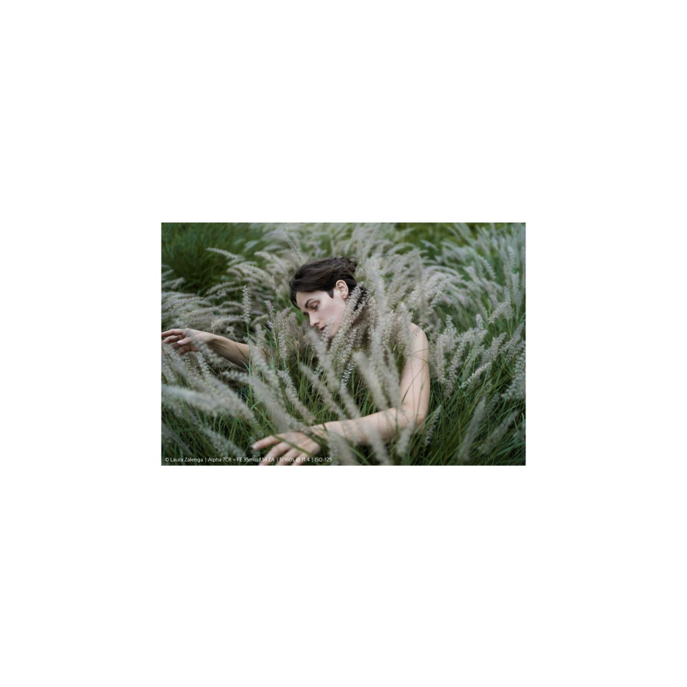 A woman lies in tall, light-colored grass. Her head is tilted slightly down.