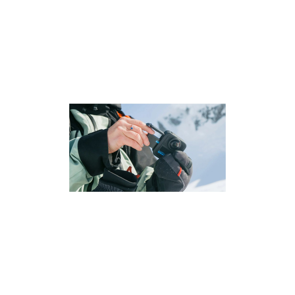 Person in Skikleidung hält eine kleine schwarze Kamera mit einem Karabiner. Berge im Hintergrund.