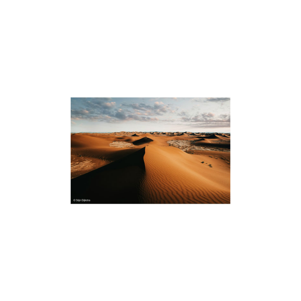 Orange sand dunes under a cloudy sky at sunset.