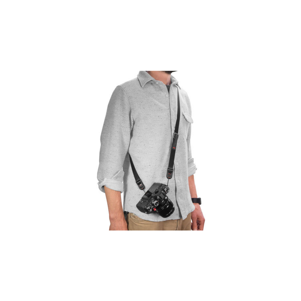 Homme portant un appareil photo en bandoulière, chemise grise, pantalon beige.