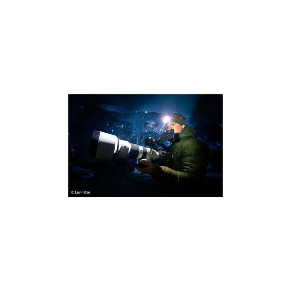 Ein Mann mit Stirnlampe fotografiert mit einer großen Kamera in einer eisigen Höhle.