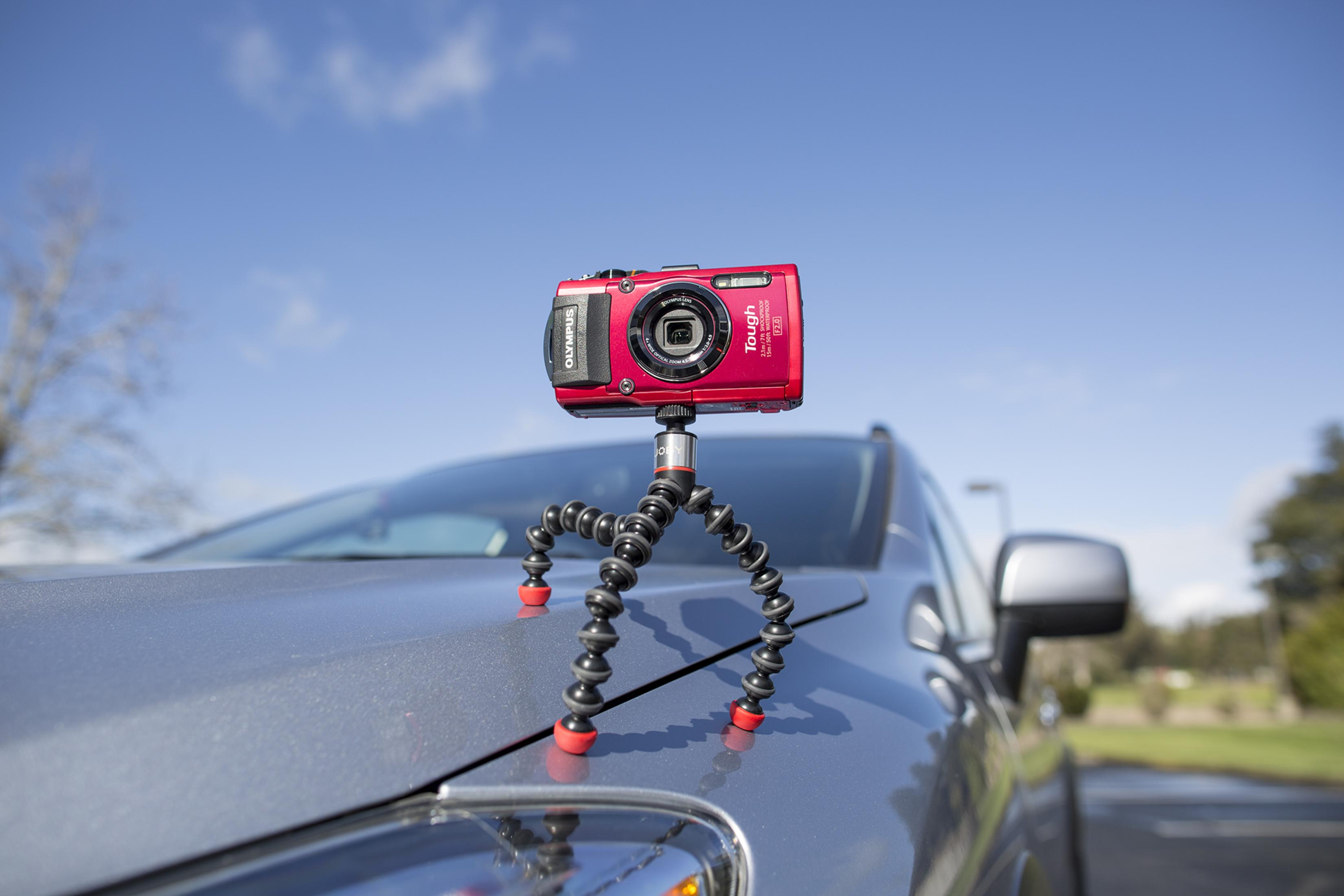 Eine rote Olympus-Kamera auf einem flexiblen Stativ auf einem Auto.