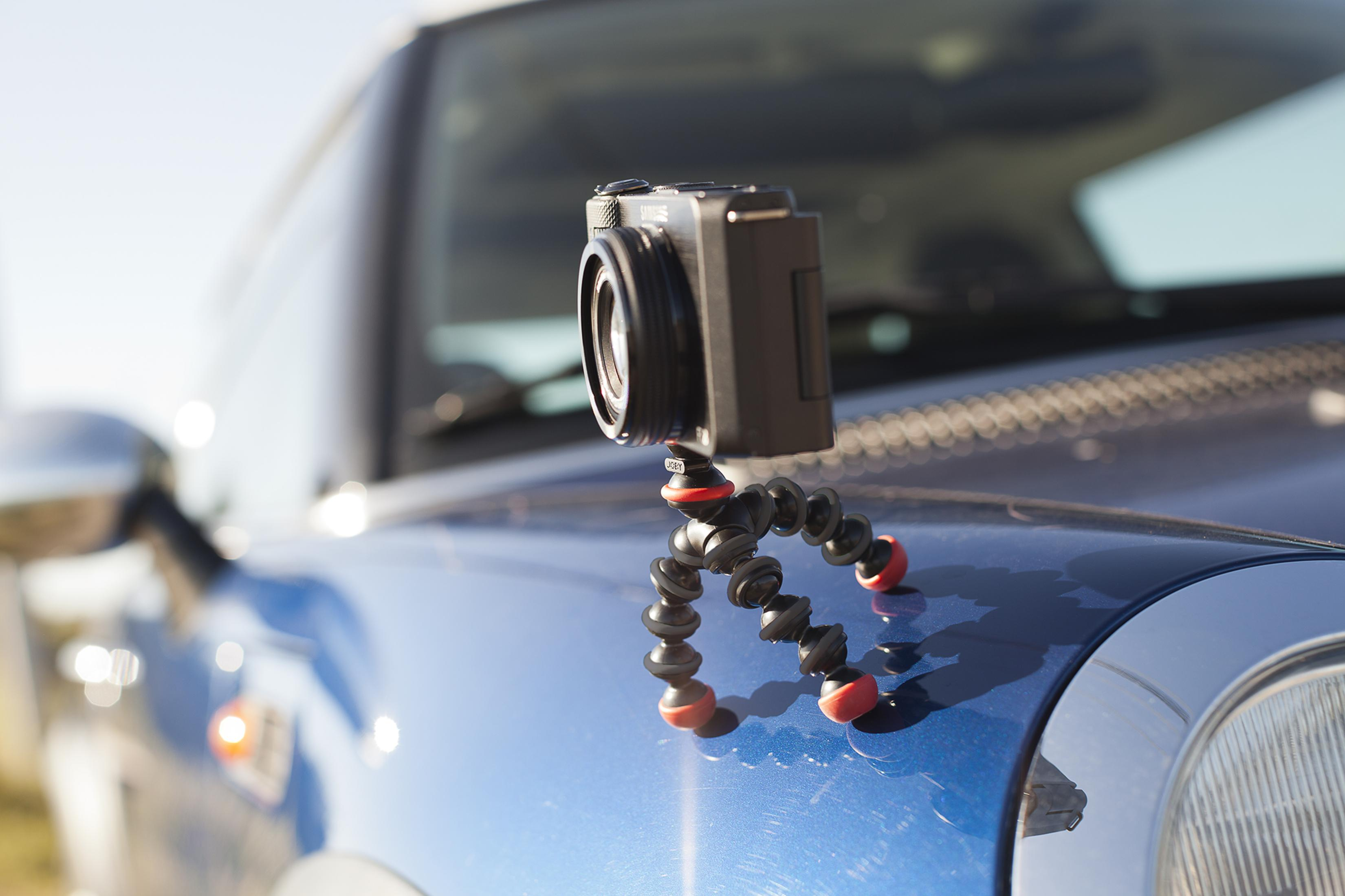 A black camera sits on a flexible tripod on a blue car.