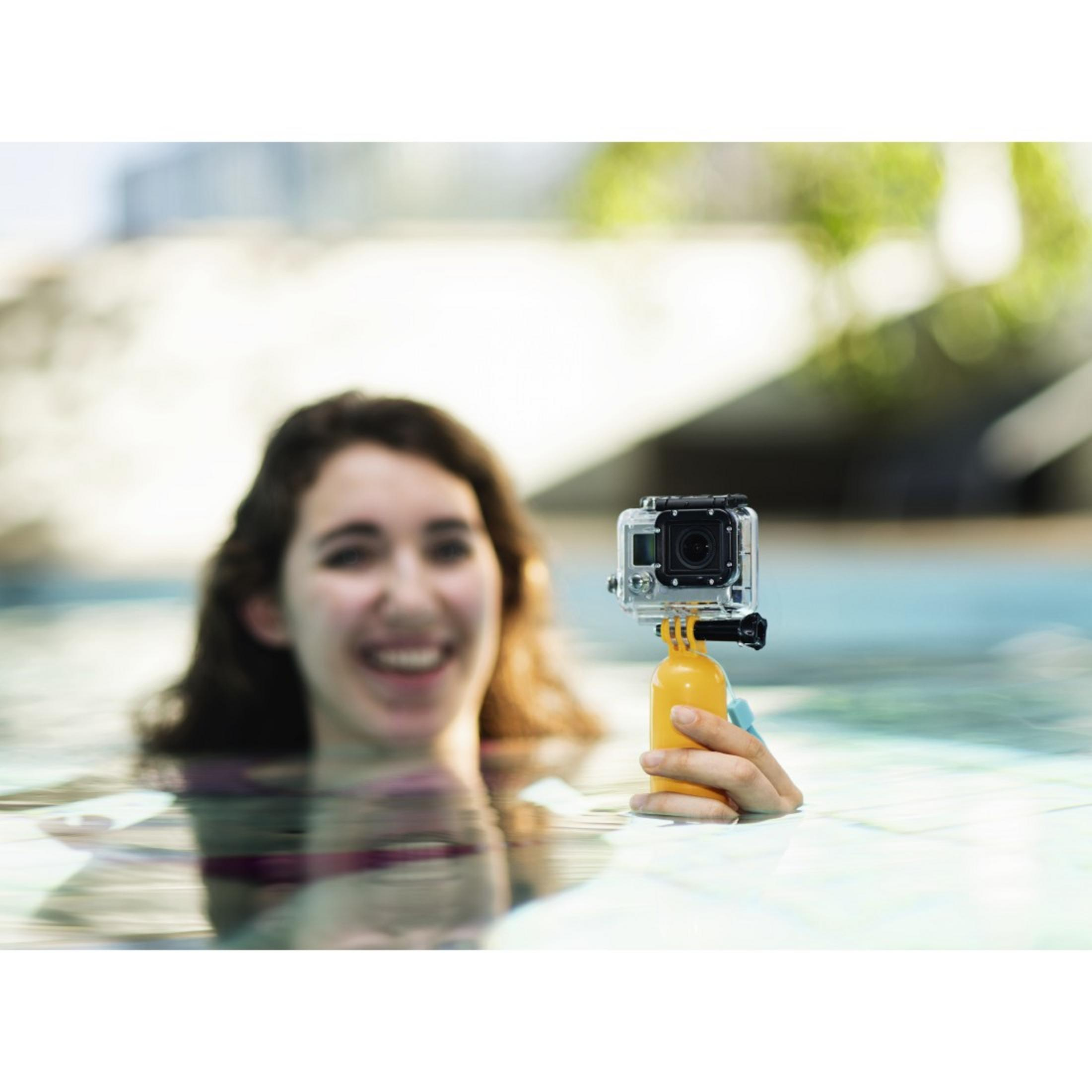 Kobieta pływa w basenie, trzymając GoPro przymocowaną do żółtej bojki.