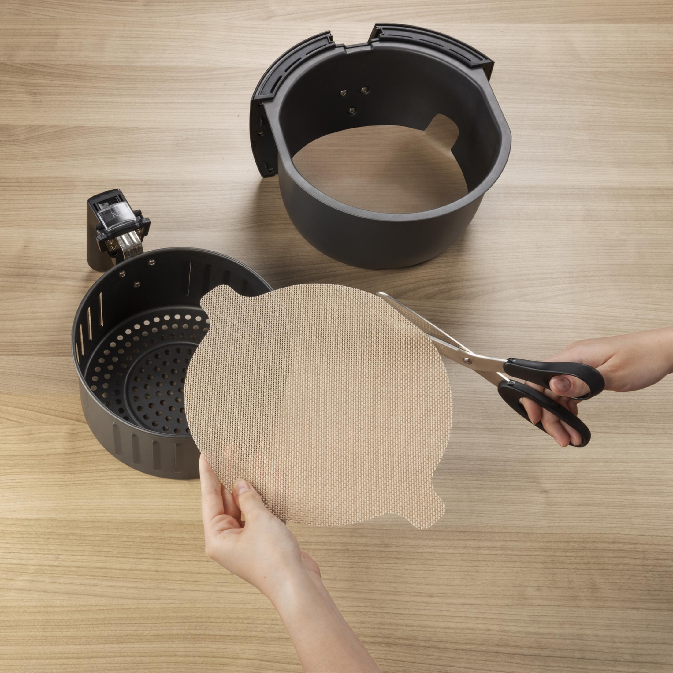 Hände schneiden runde Backpapier-Einlage für Heißluftfritteuse mit Schere.