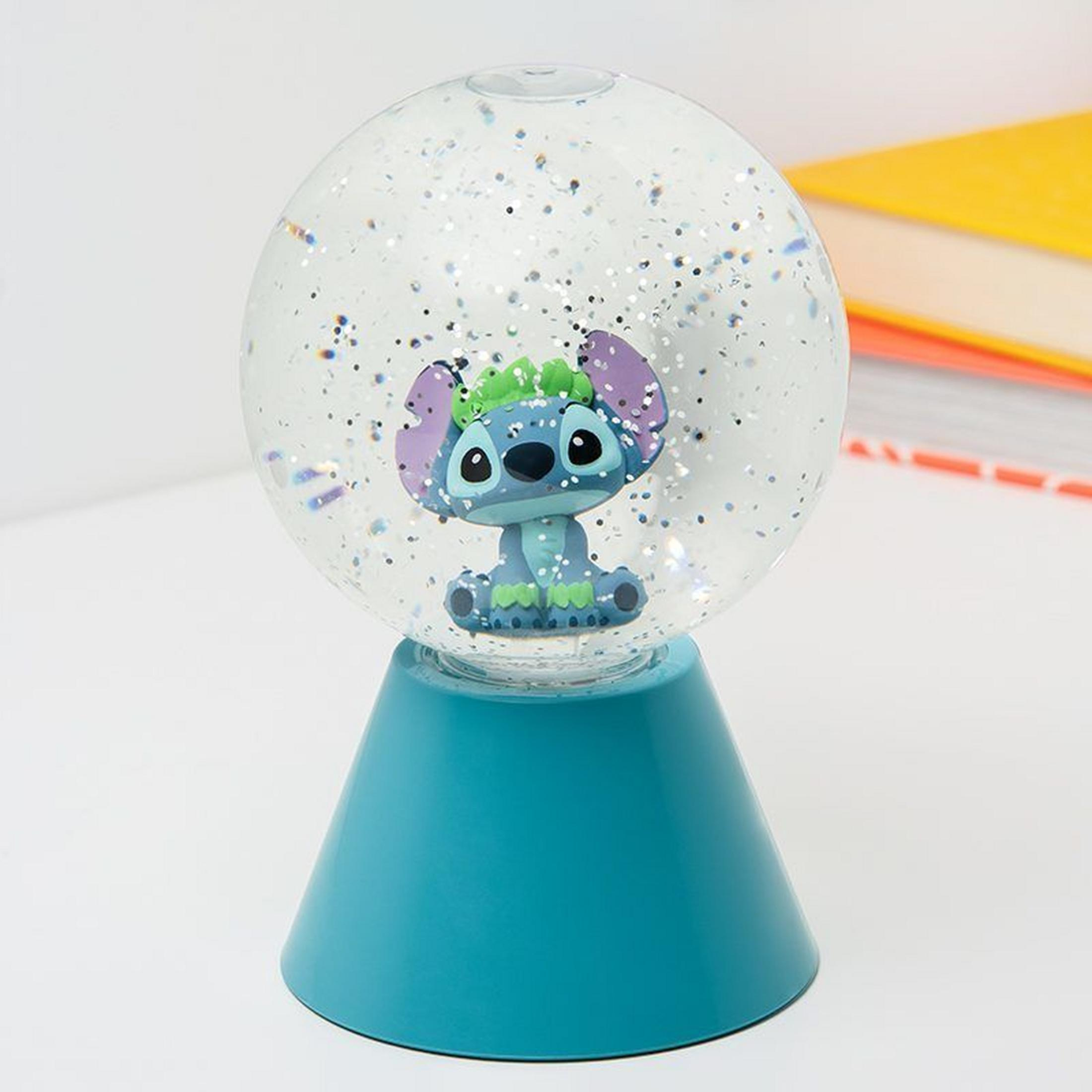 Niebieski Stitch z zielonymi włosami siedzi w kuli śnieżnej z brokatem.