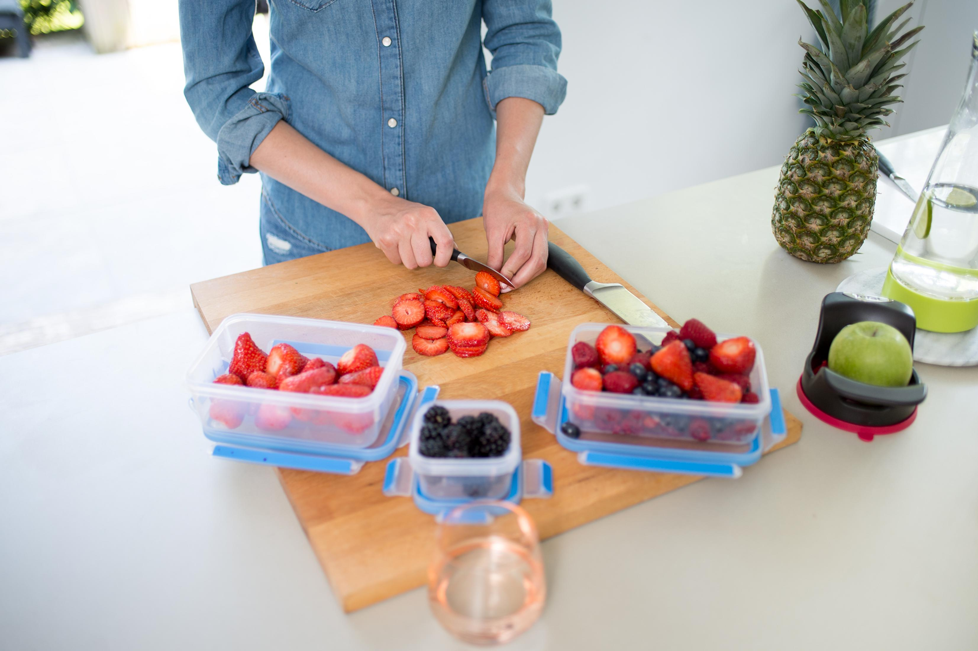 Una persona corta fresas en una tabla de cortar, con bayas y una piña cerca.