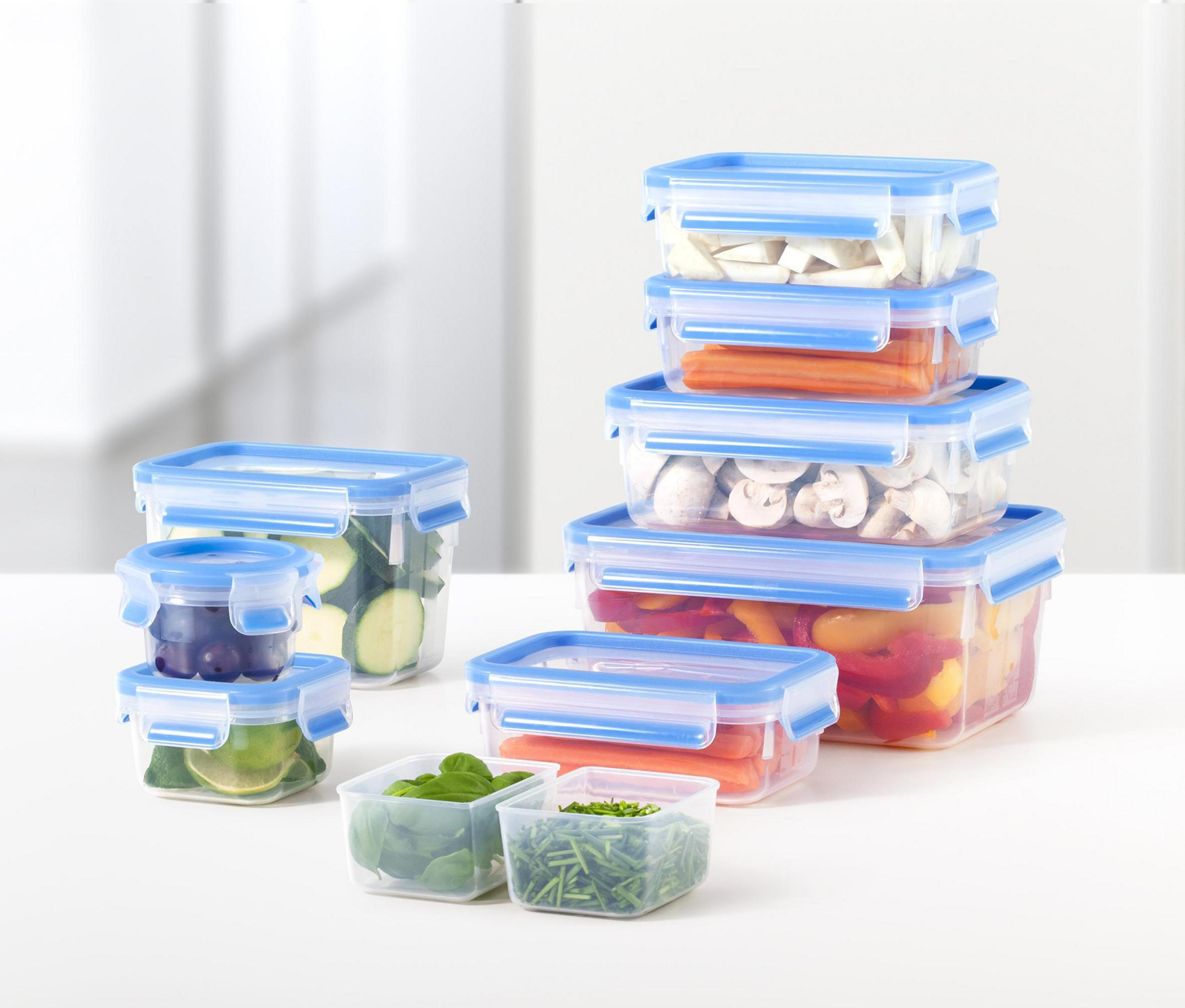 Múltiples recipientes transparentes con tapas azules, llenos de frutas y verduras.