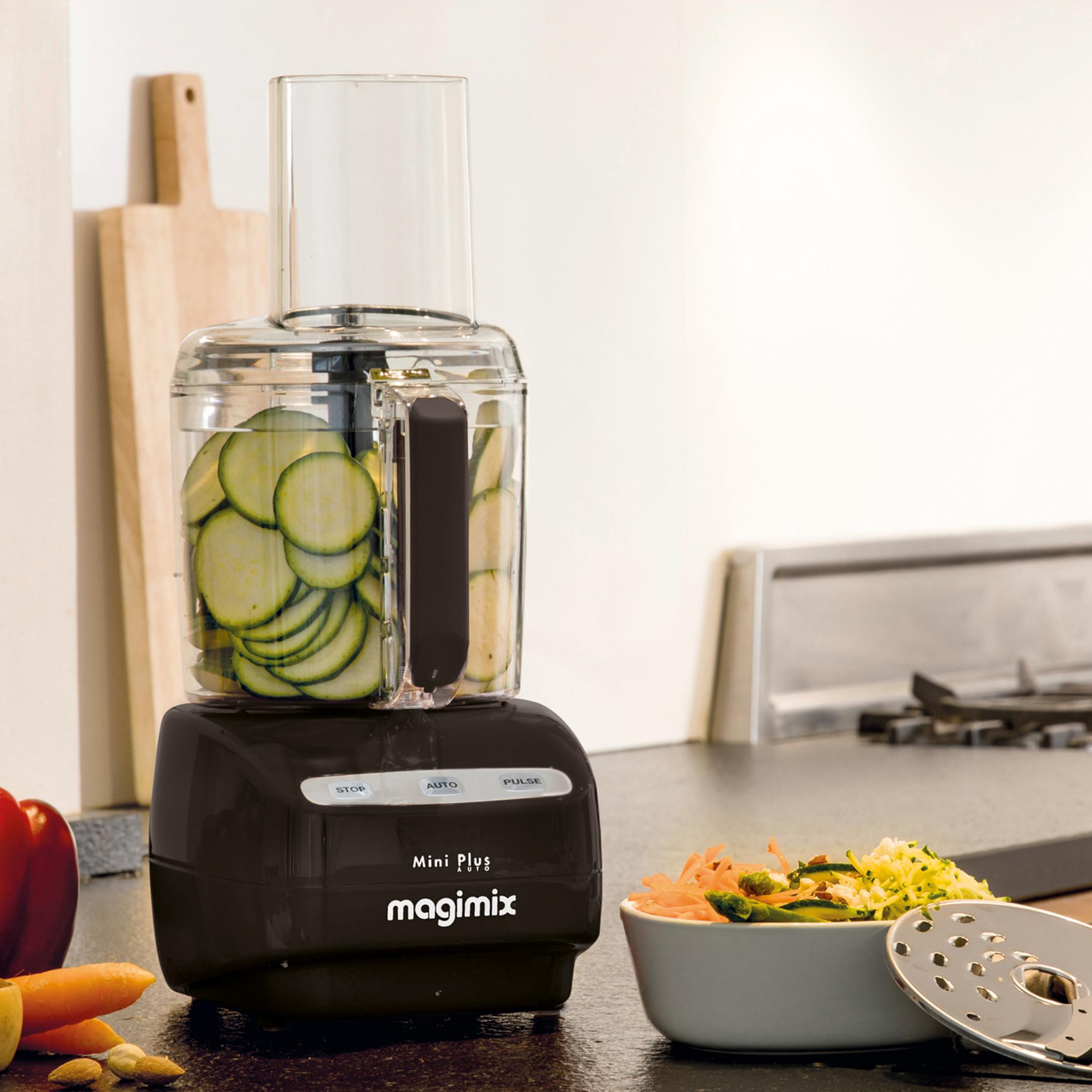 Een zwarte keukenmachine met plakjes courgette en een kom salade.