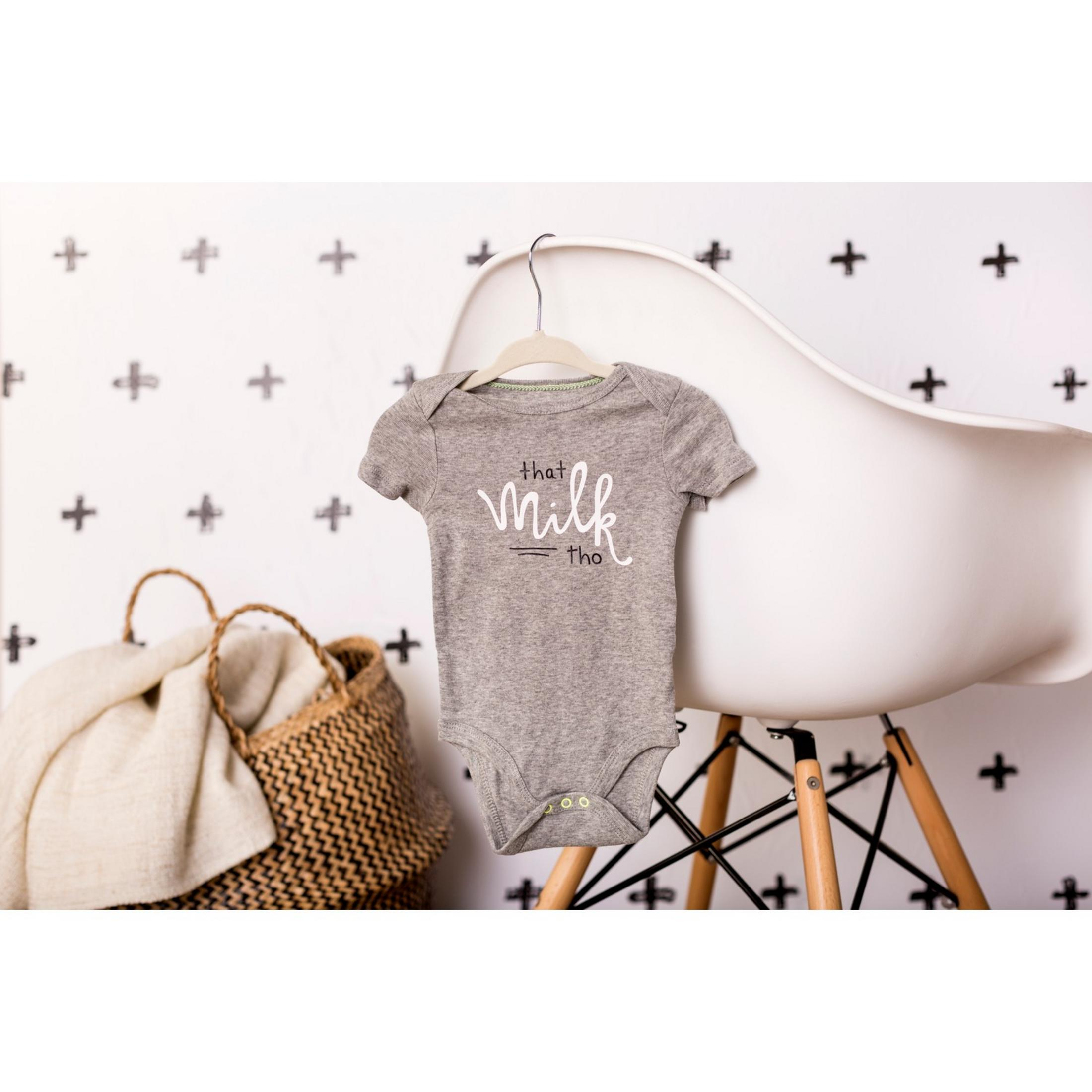Grauer Baby-Strampler mit Aufschrift „that milk tho“ hängt auf einem Stuhl.