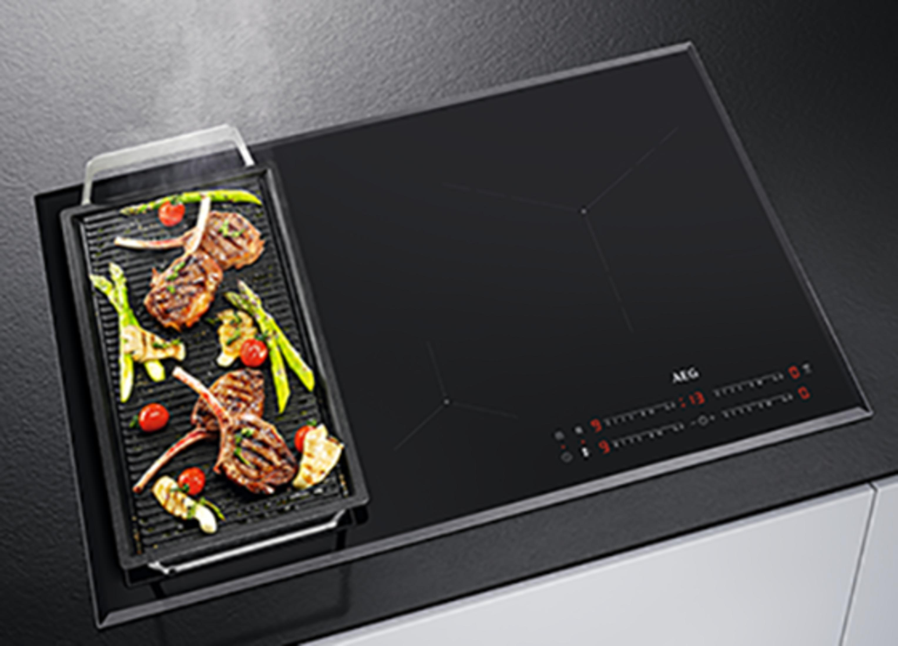 Una parrilla con carne, espárragos y tomates en una placa de inducción negra.