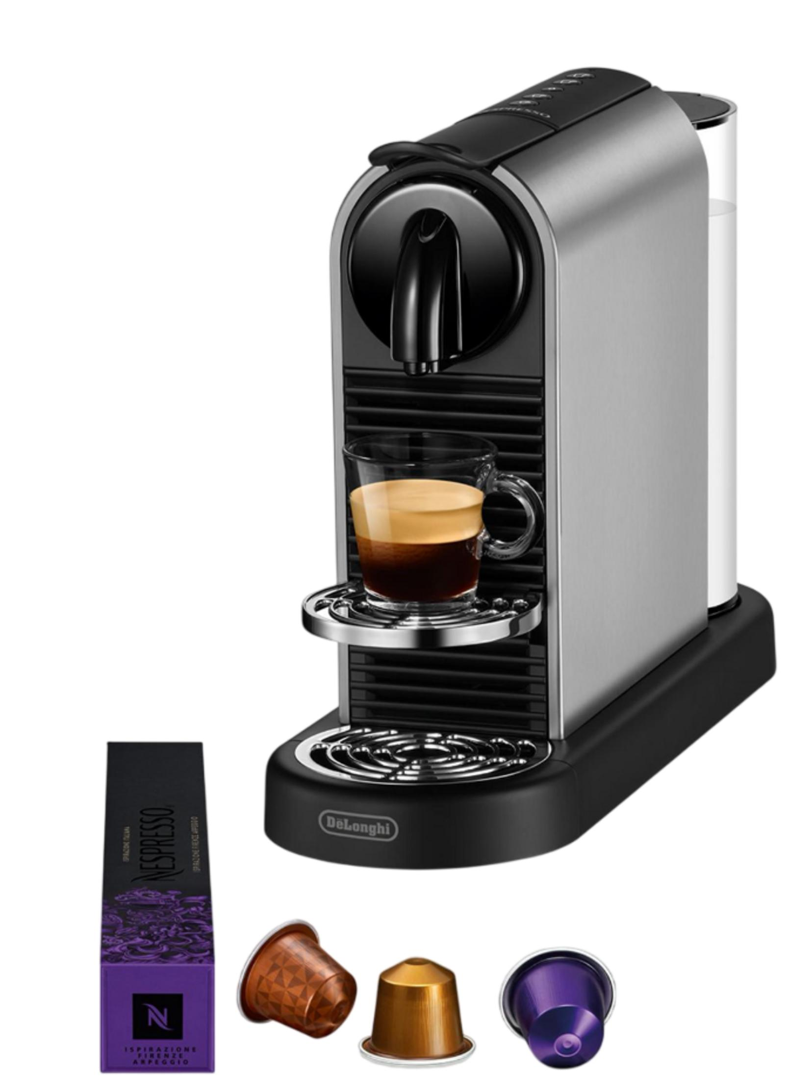 Una cafetera plateada con una taza de espresso, cápsulas Nespresso y un paquete.