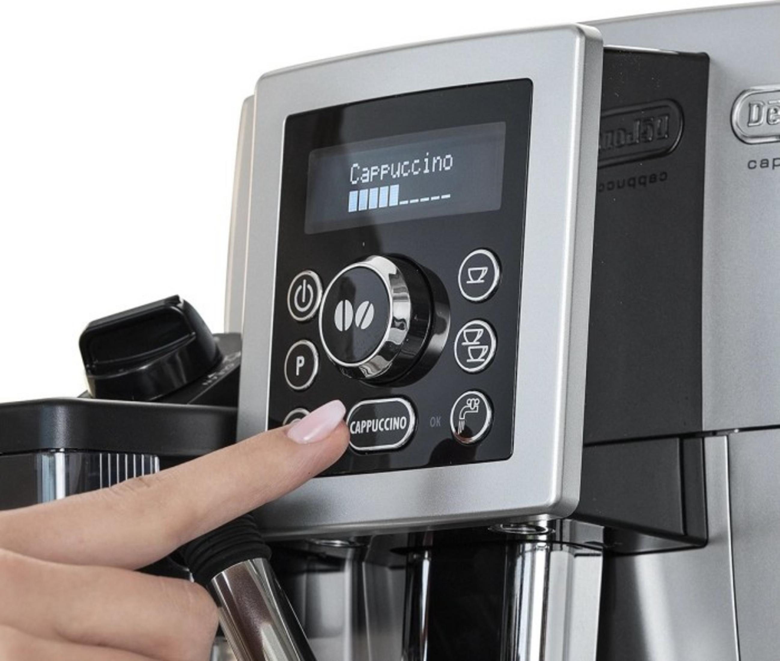 Una mano presiona el botón de capuchino en una cafetera plateada con pantalla.