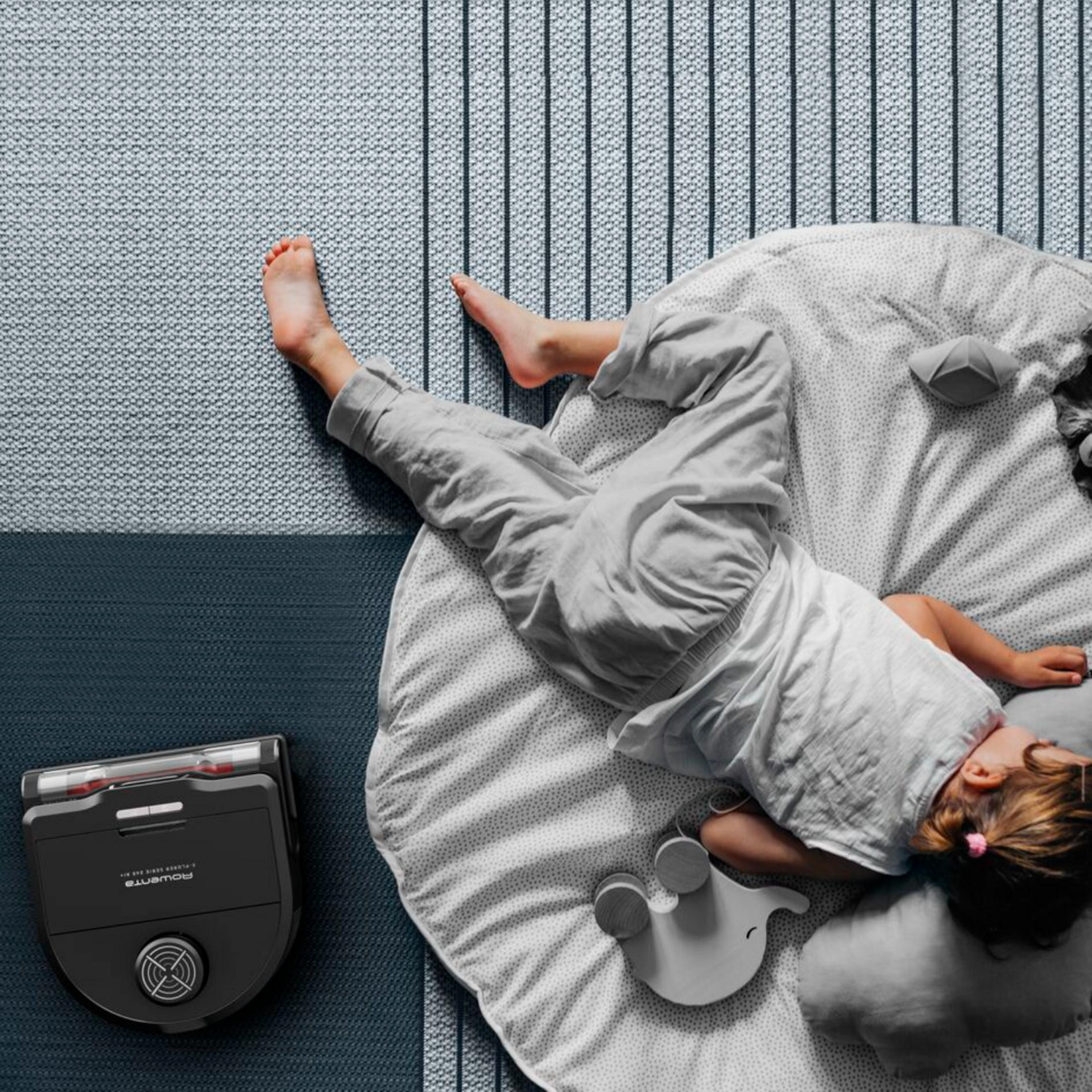 Un niño duerme en una alfombra de juegos junto a un robot aspirador.