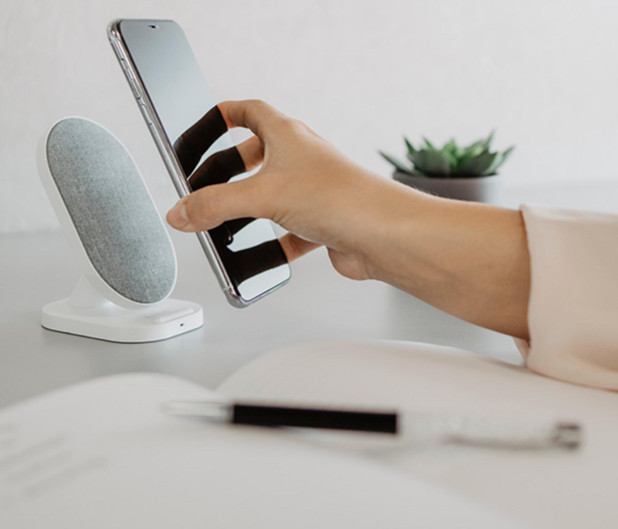 Eine Hand hält ein Smartphone über eine weiße Ladestation.