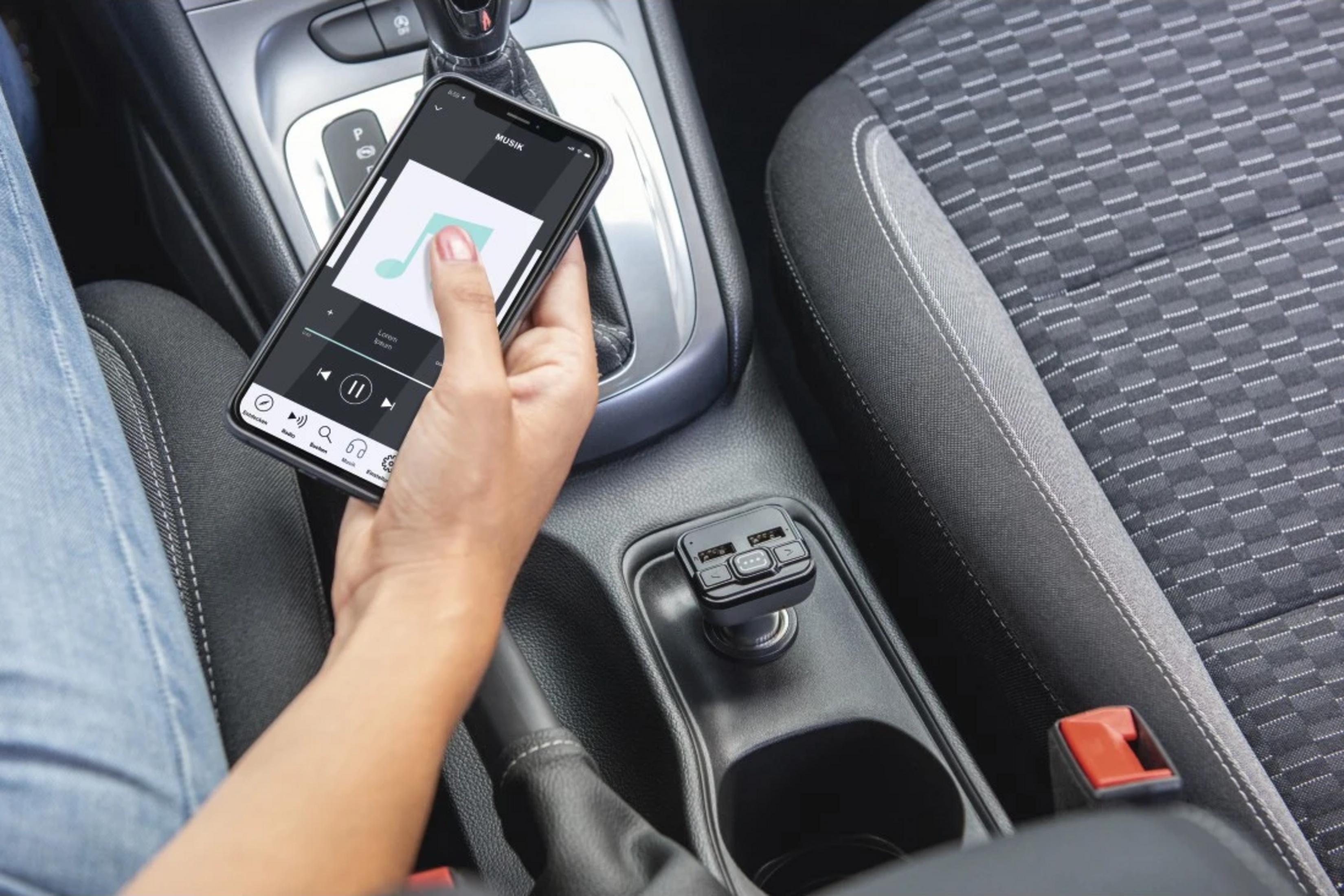 Hand hält Smartphone mit Musik-App im Auto, neben Schalthebel und Ladeadapter.