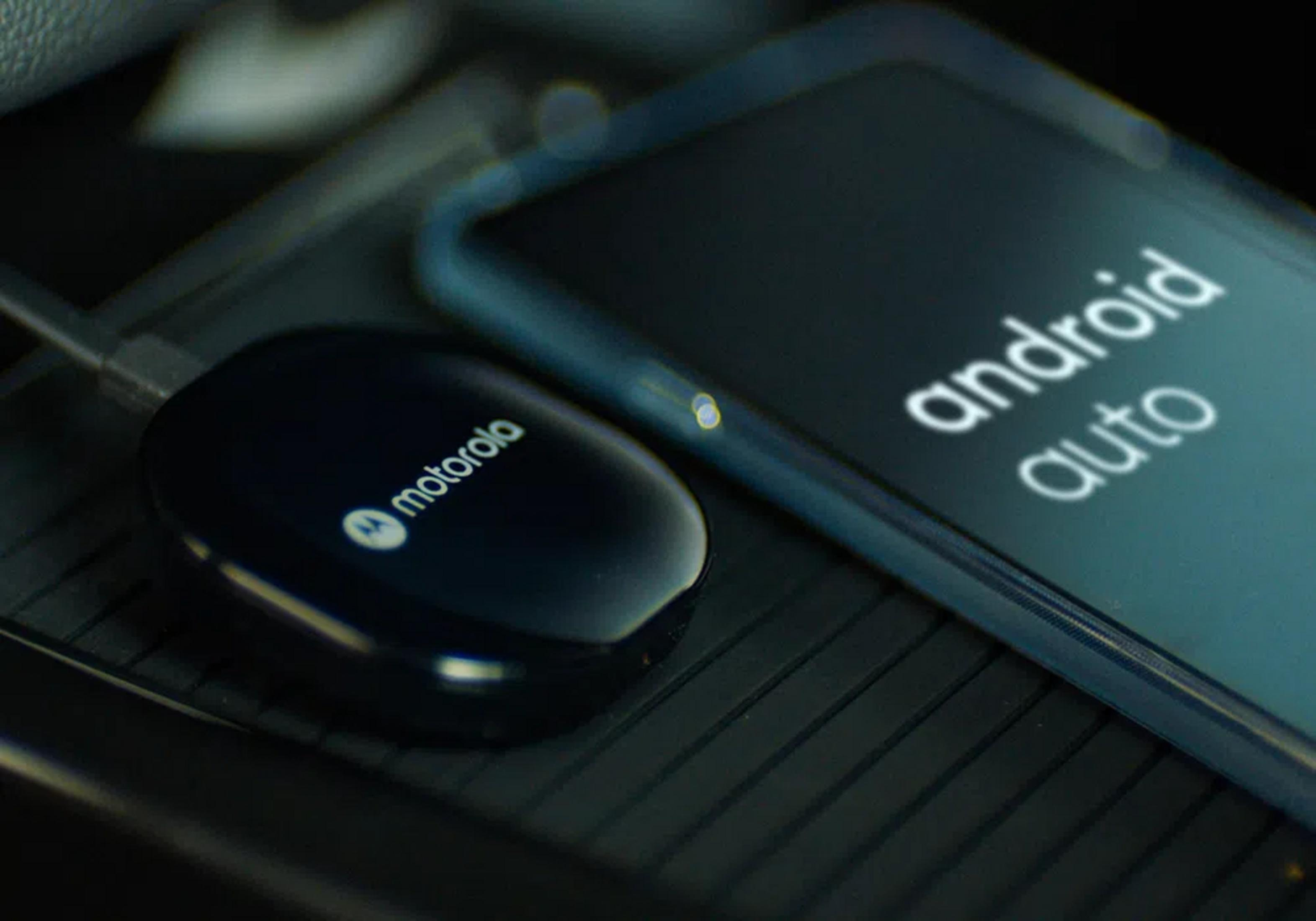 Un dongle Motorola Android Auto junto a un smartphone en un coche.