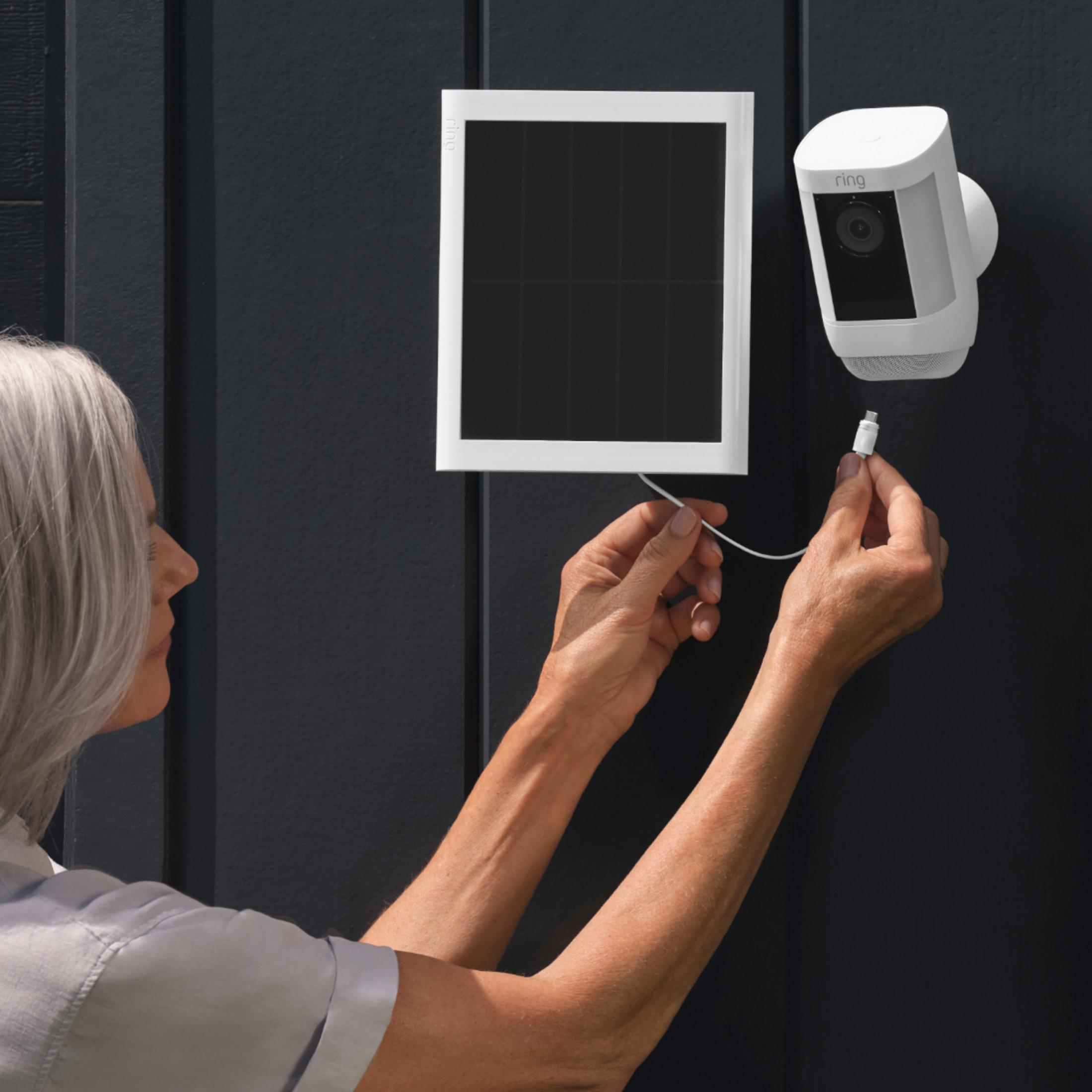 Eine Person schließt ein weißes Kabel an eine Ring-Überwachungskamera und ein Solarpanel an.