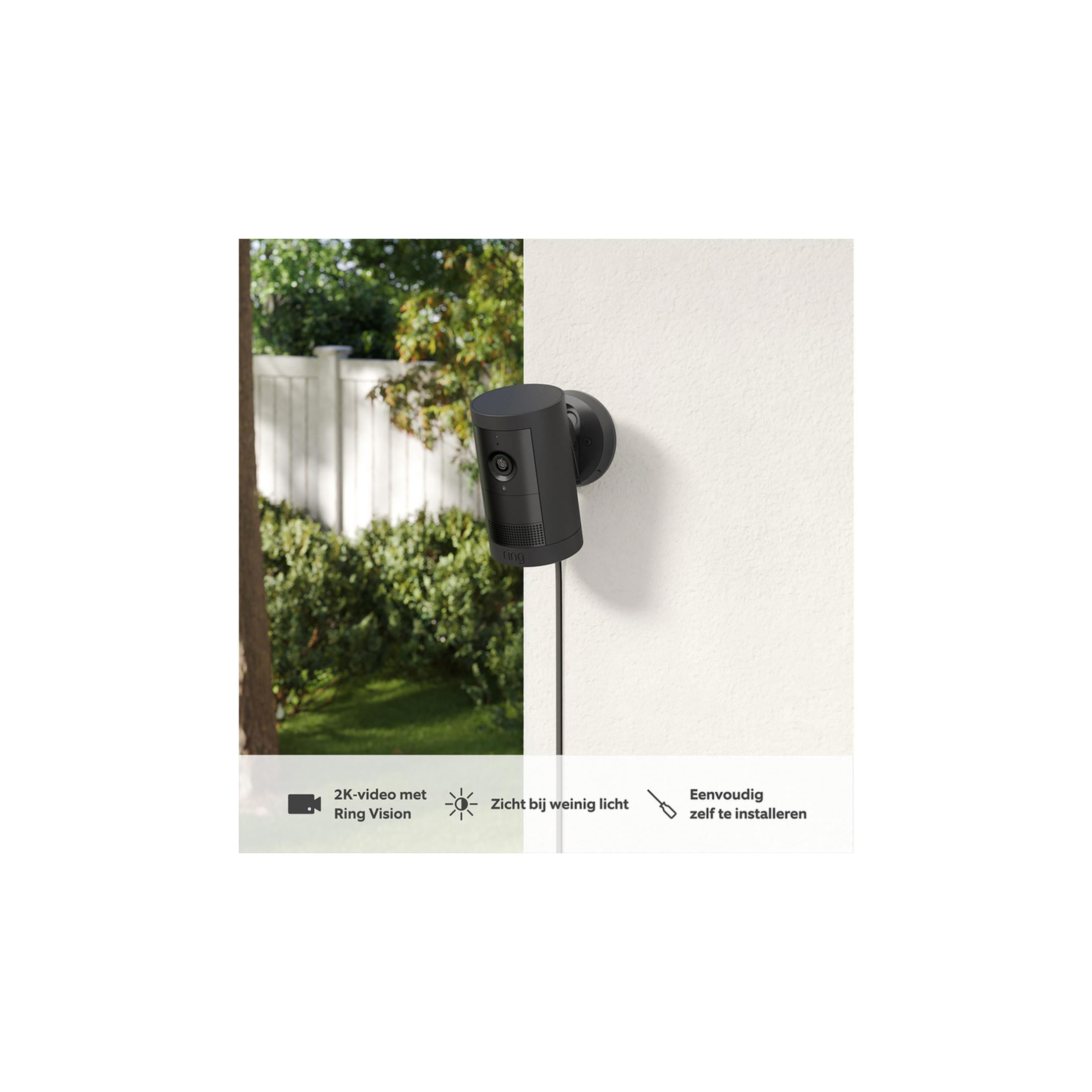 Una telecamera di sicurezza nera è montata su un muro bianco. Si vede vegetazione all'esterno.