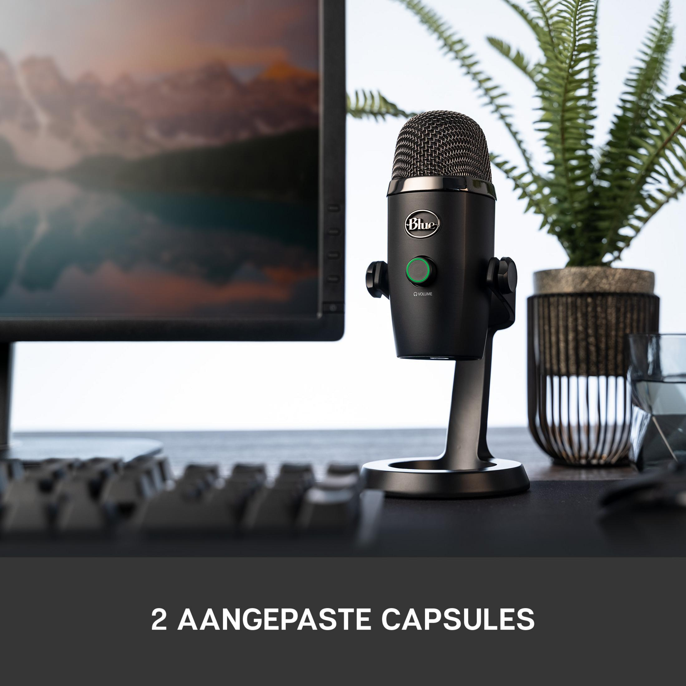 Ein schwarzes Mikrofon steht auf einem Schreibtisch neben einem Monitor.