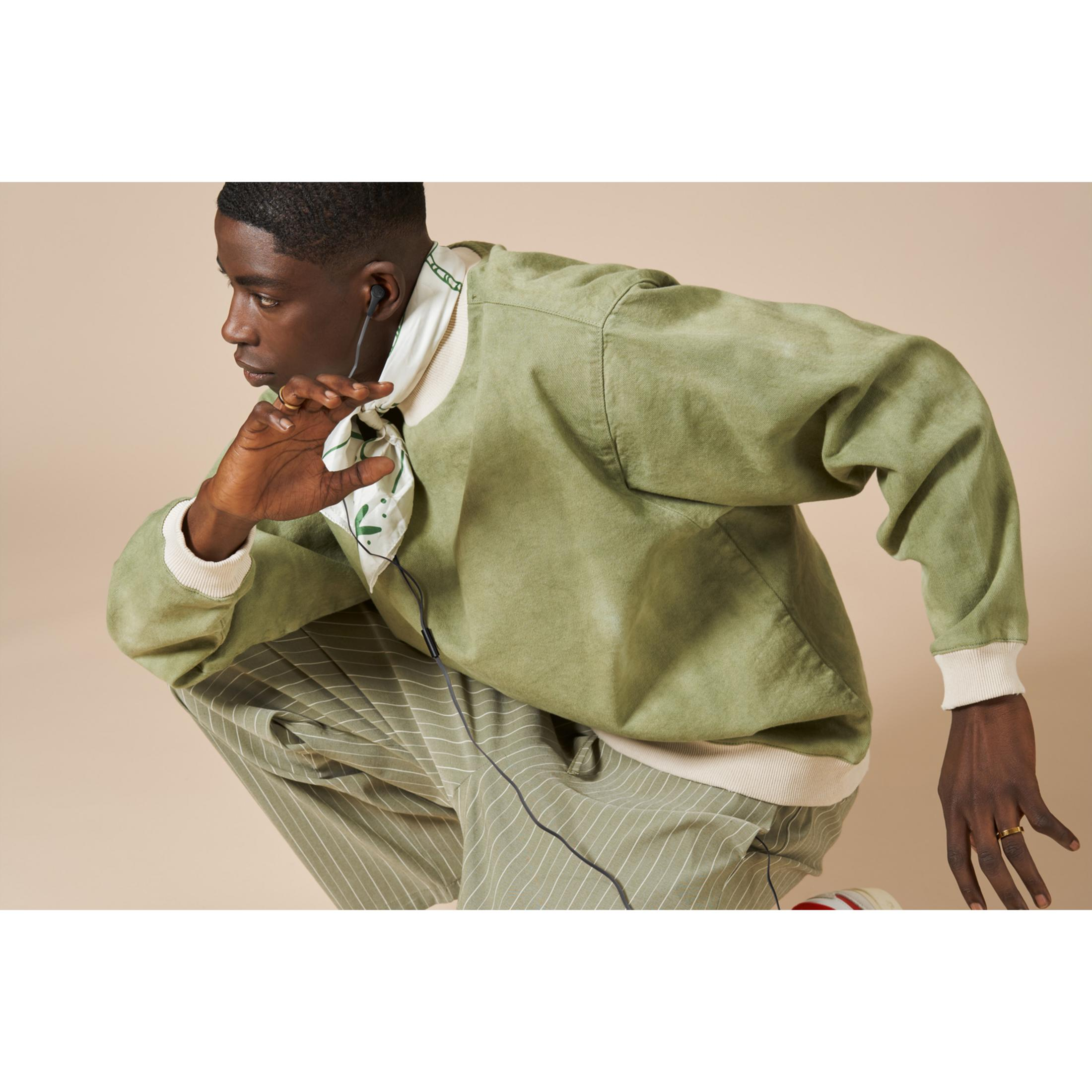 Een man in groene kleding knielt, draagt oordopjes en houdt een sjaal vast.