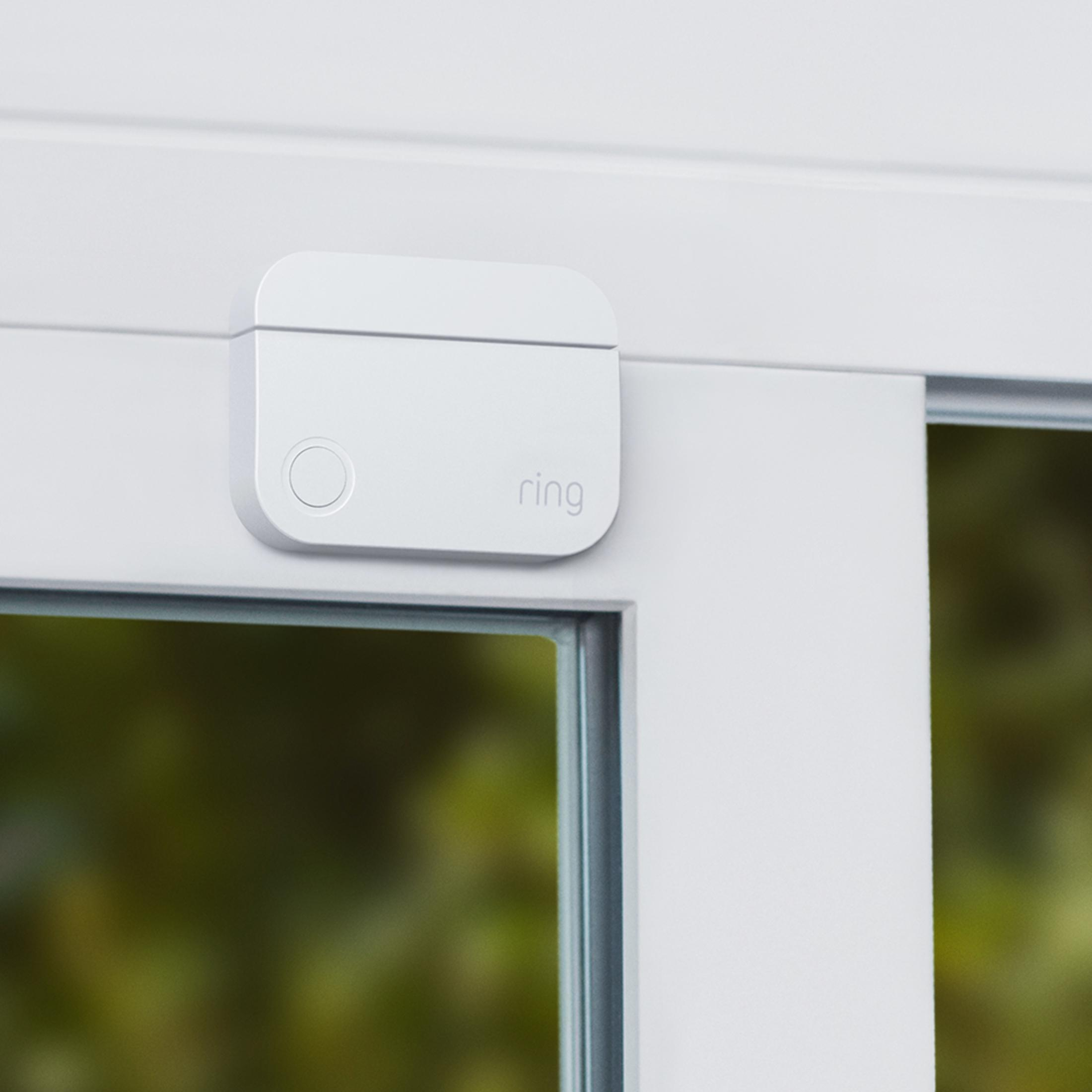 Ein weißer Ring-Kontaktsensor ist an einem weißen Fensterrahmen befestigt. Draußen ist grüne Laub zu sehen.
