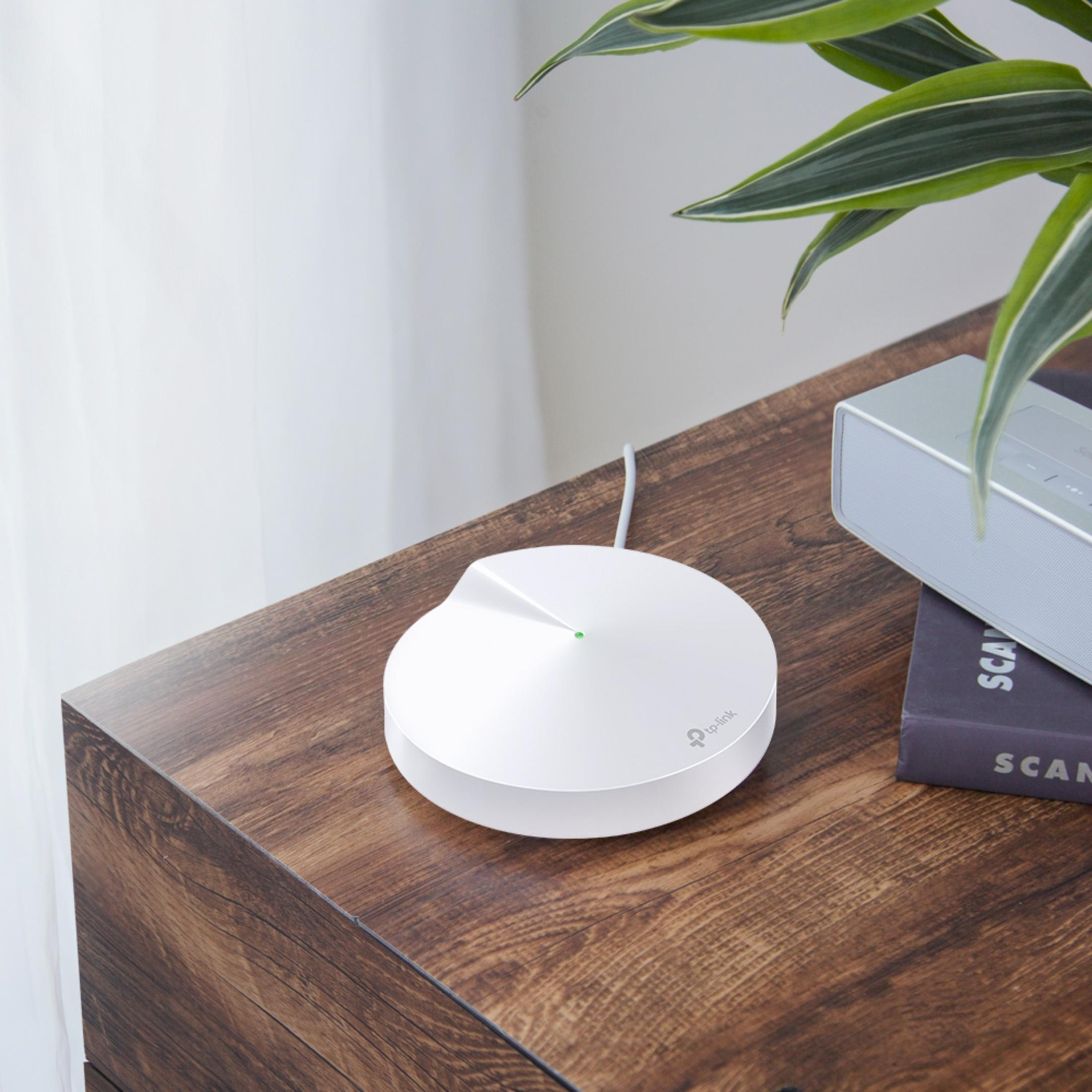 Biały router TP-Link z zielonym światłem stoi na drewnianym stole obok głośnika.