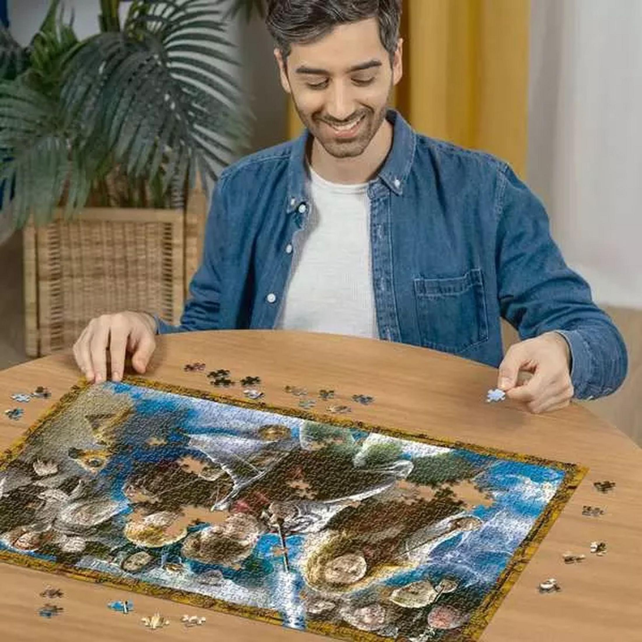 Mężczyzna siedzi przy drewnianym stole i układa puzzle. Trzyma mały element układanki.