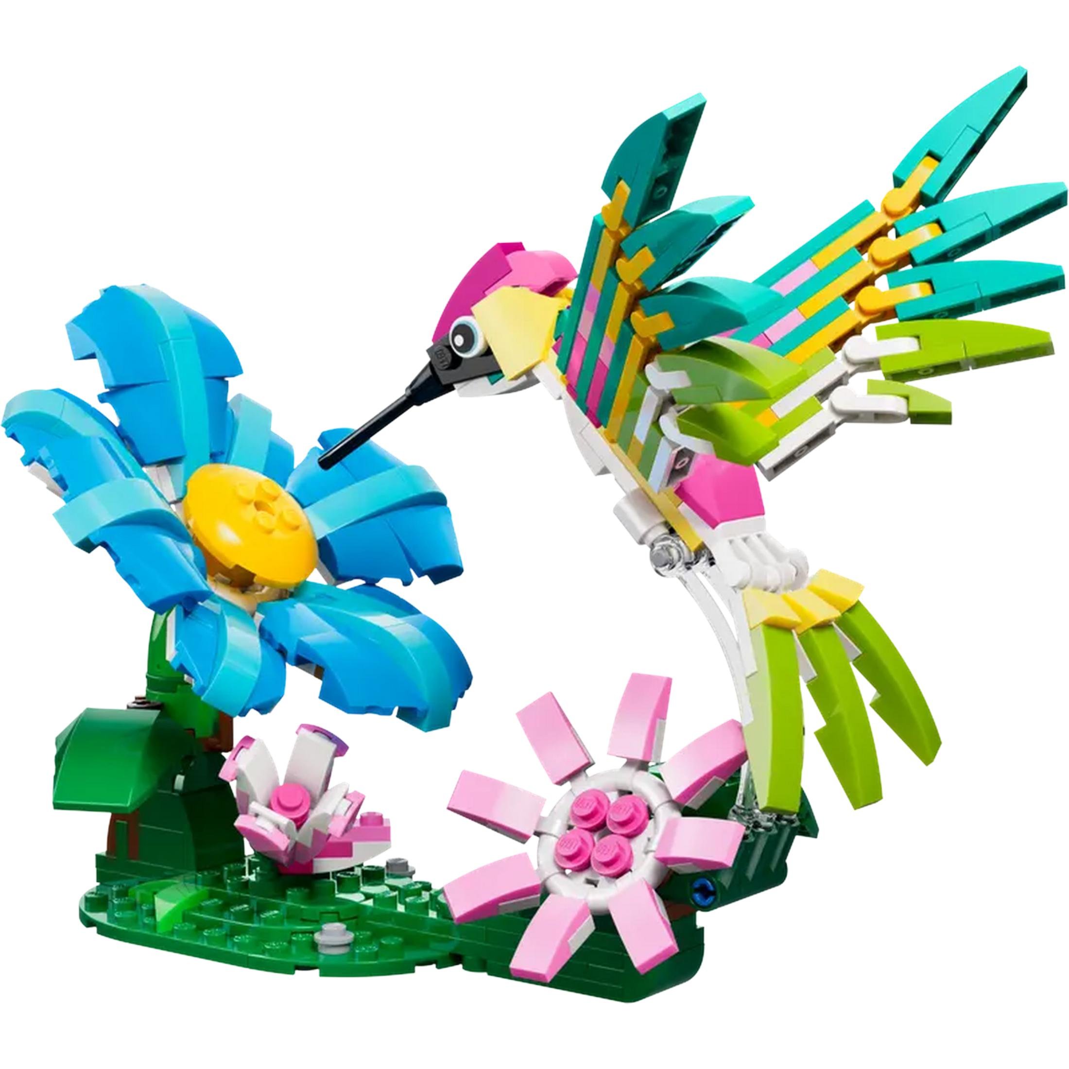 Kolorowy koliber Lego przy niebieskim kwiecie na zielonej podstawie.
