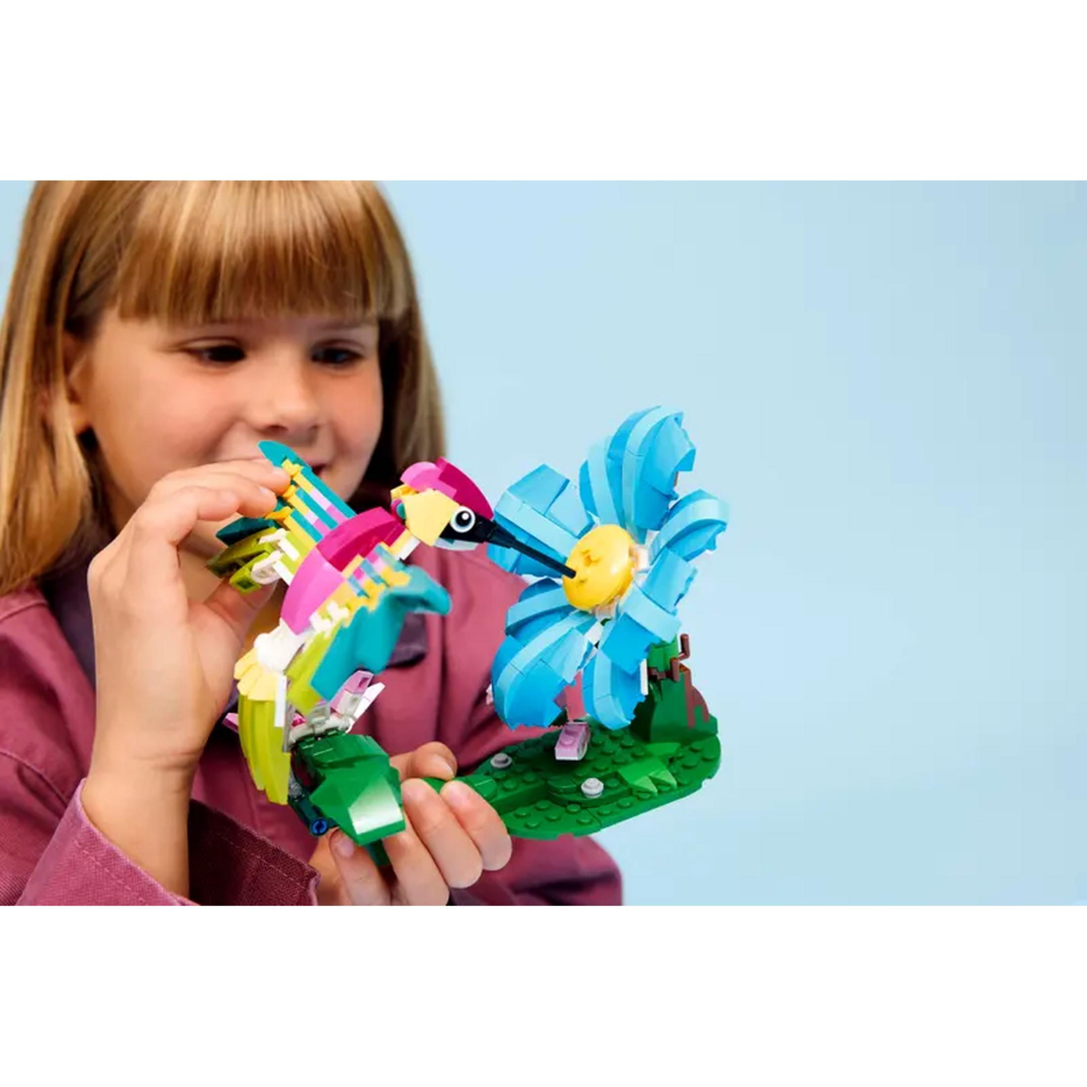 Dziecko trzyma kolorowego Lego kolibryka zbliżającego się do niebieskiego kwiatu.