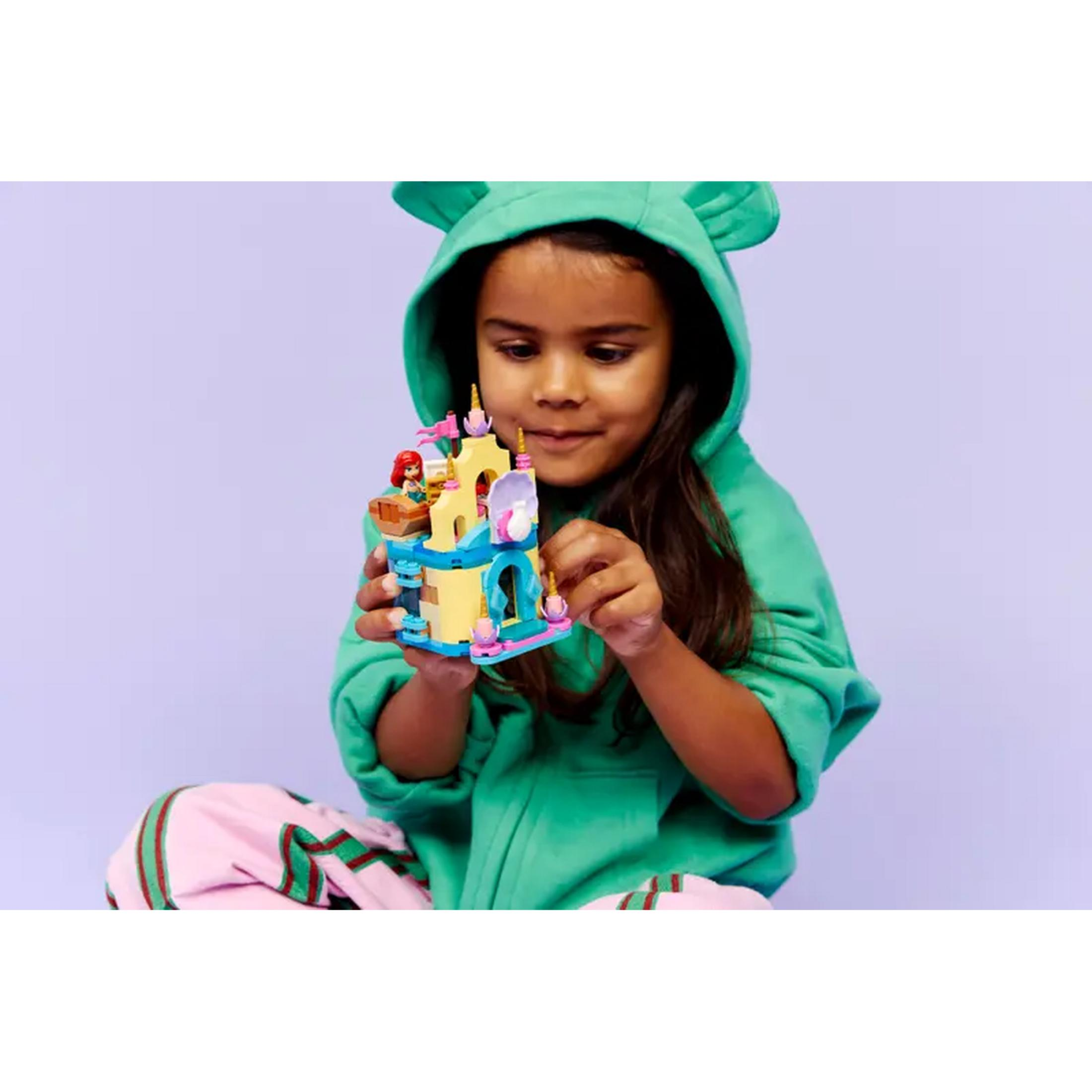 Una niña con sudadera verde y orejas sostiene un castillo de Lego colorido.