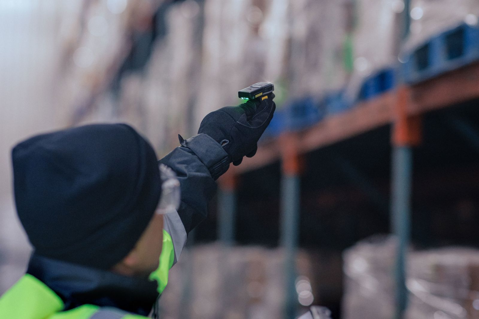 Una mano guantata tiene un piccolo scanner nero con luce verde in un magazzino.
