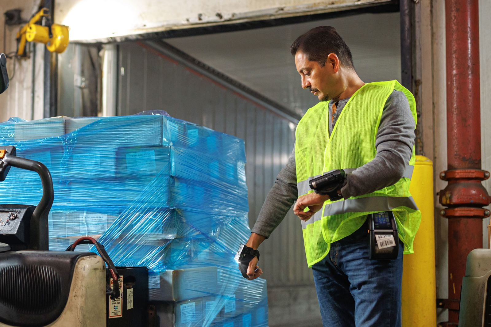 Operaio magazziniere con gilet neon scansiona pallet avvolti in blu.