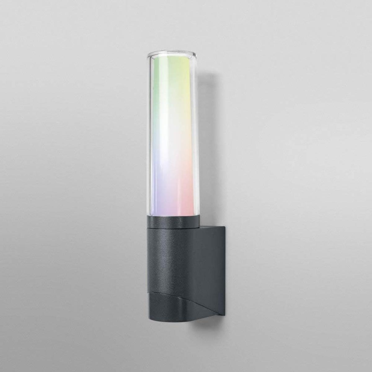 Eine dunkle Wandleuchte mit einem zylindrischen Glasdiffusor, der in Regenbogenfarben leuchtet.