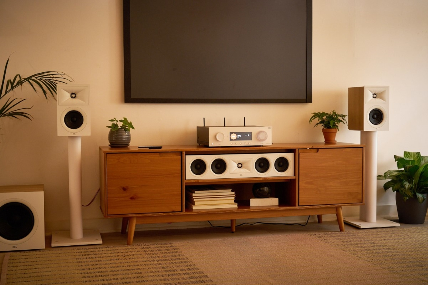 Białe głośniki na stojakach obok drewnianej szafki z telewizorem i elektroniką.