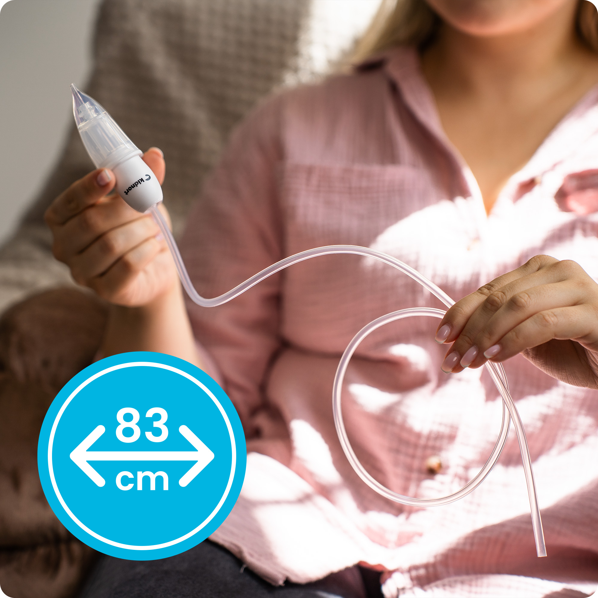 Ręka trzyma biały i przezroczysty aspirator do nosa z rurką. Niebieskie kółko pokazuje 83 cm.