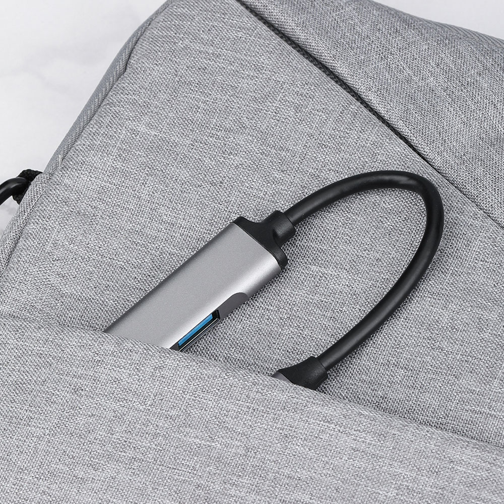 Szary koncentrator USB-C z czarnym kablem schowany w szarej torbie materiałowej.